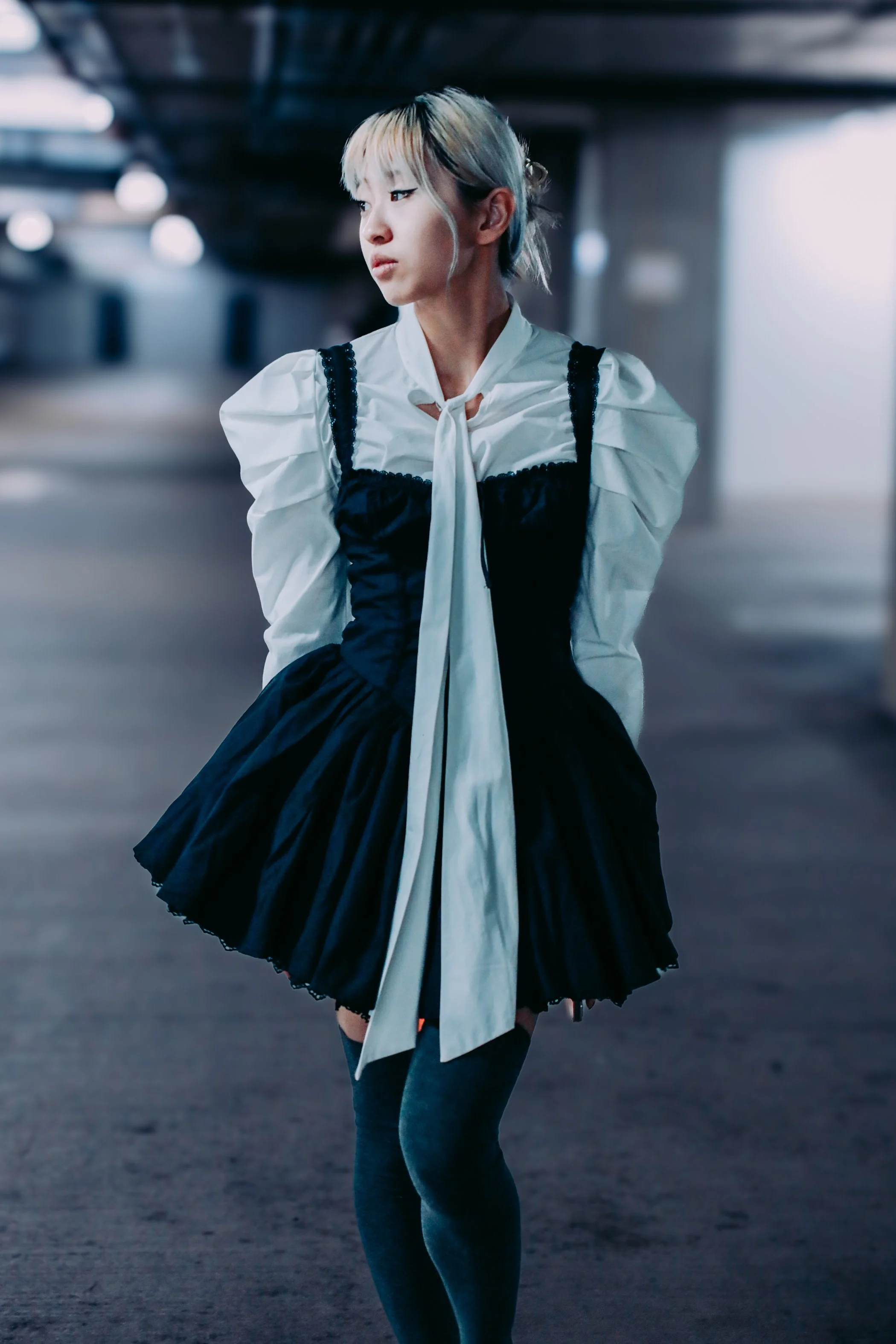 Young woman with short, multi-colored hair in an edgy, modern outfit standing in an urban parking garage.