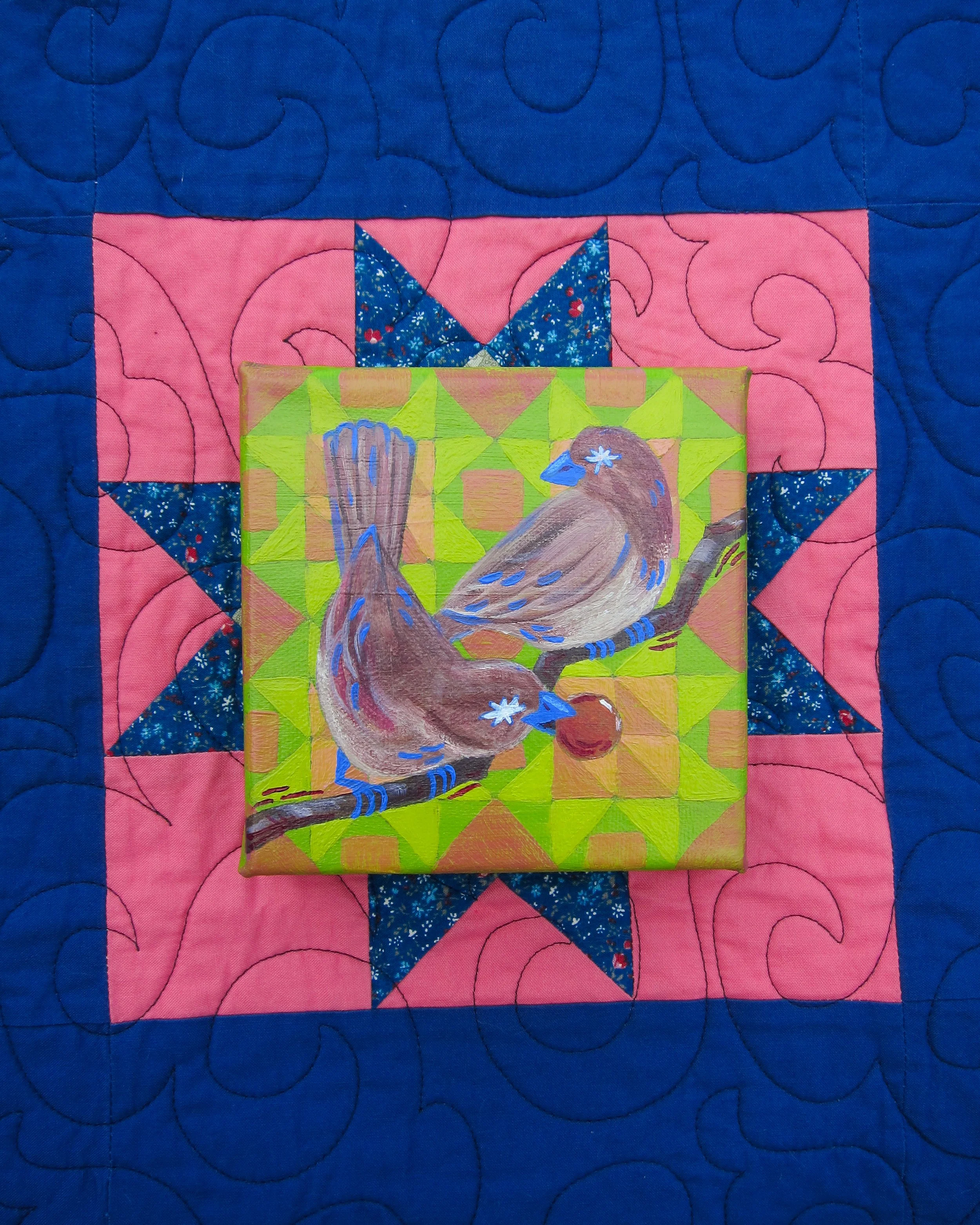 A colorful quilt with a pink background and blue quilting pattern, featuring a small painting of a bird perched on a branch with a green and yellow geometric background placed on the quilt.