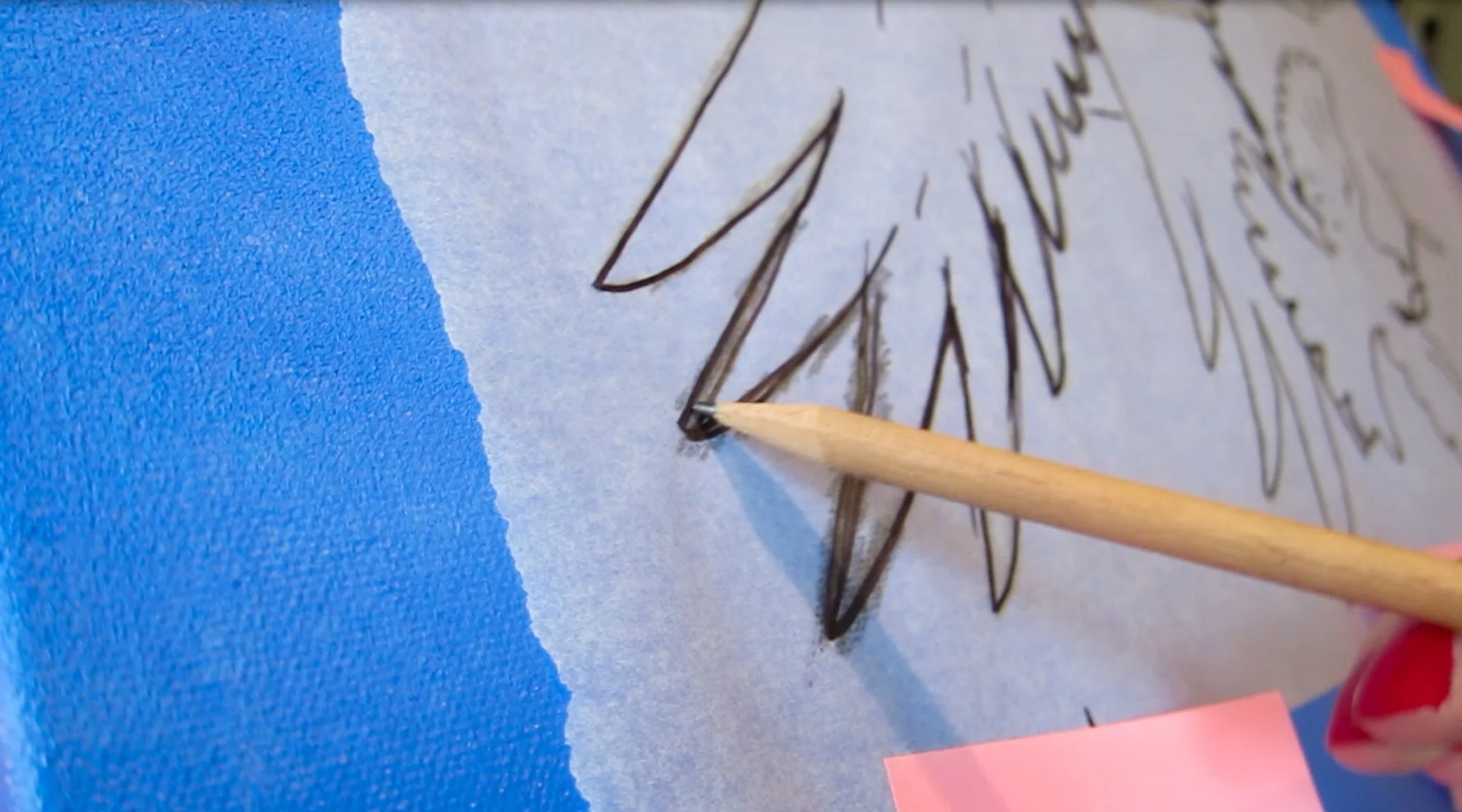 A close-up of a pencil drawing a large flower on watercolor paper, with blue paint on the left side.