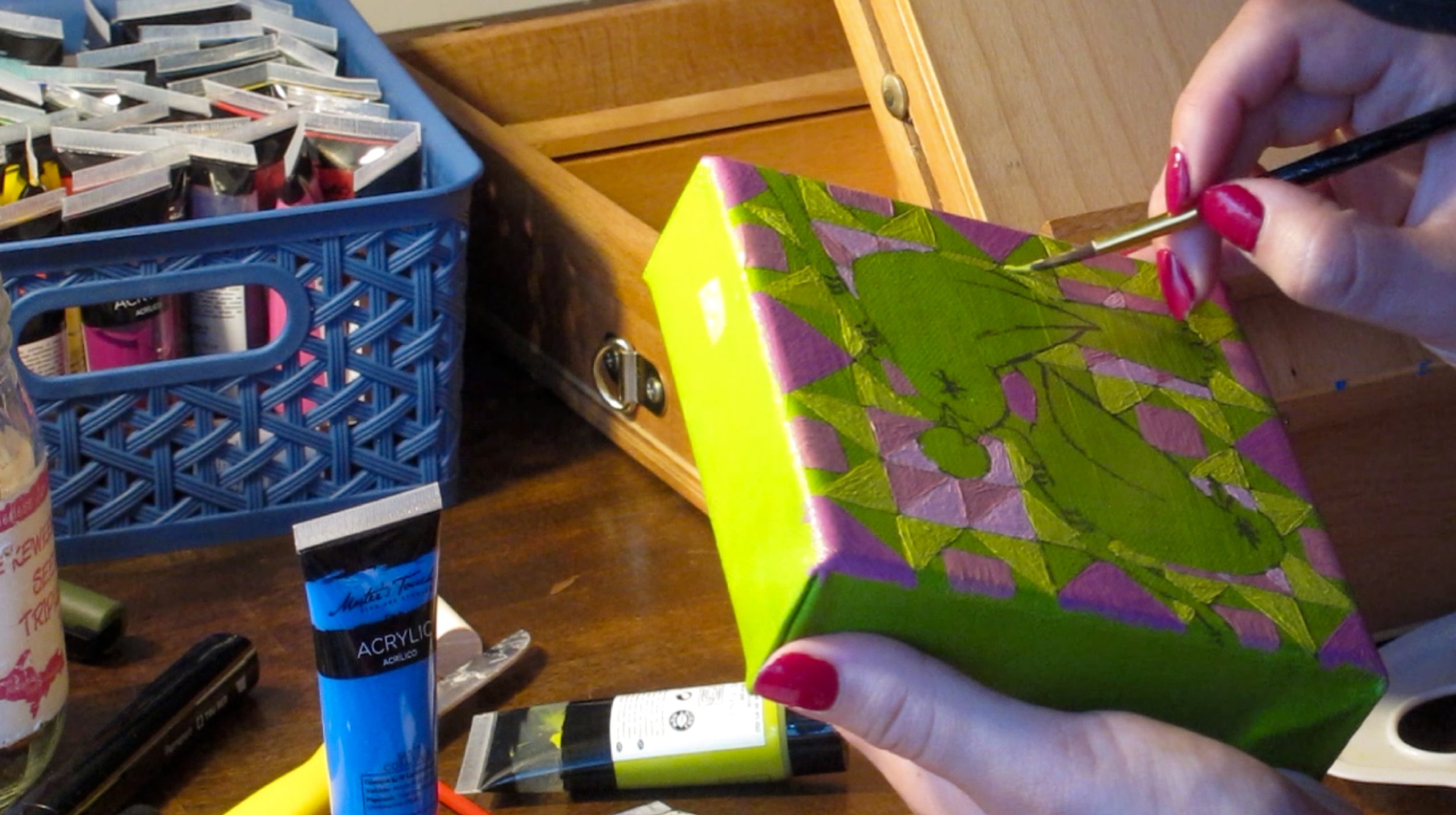Hand painting a colorful box with green, pink, and yellow geometric patterns.