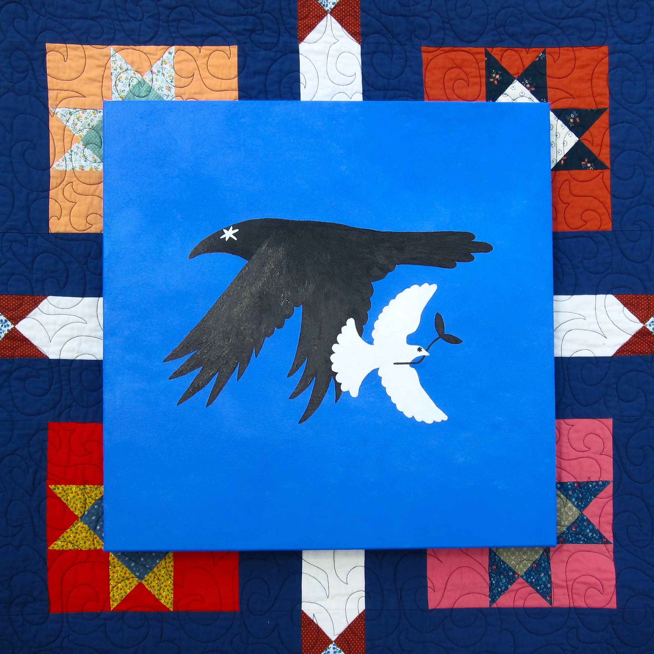 Close-up of a quilt with a central blue square, a black bird with a white tail and a small white star on its head, and colorful patchwork borders with red, white, blue, and patterned fabrics, all on a quilted background.
