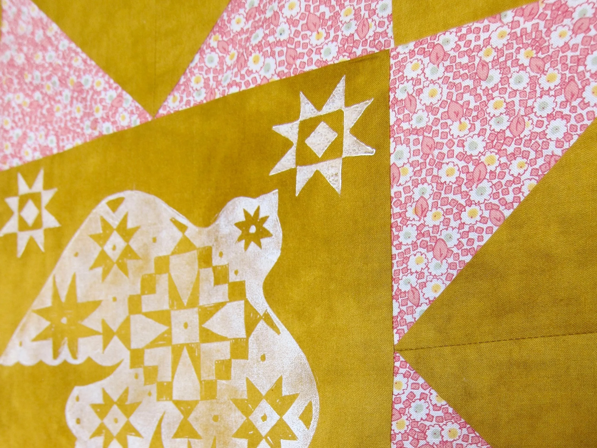 Close-up of a quilt featuring yellow, pink, and white fabric with star and floral patterns.