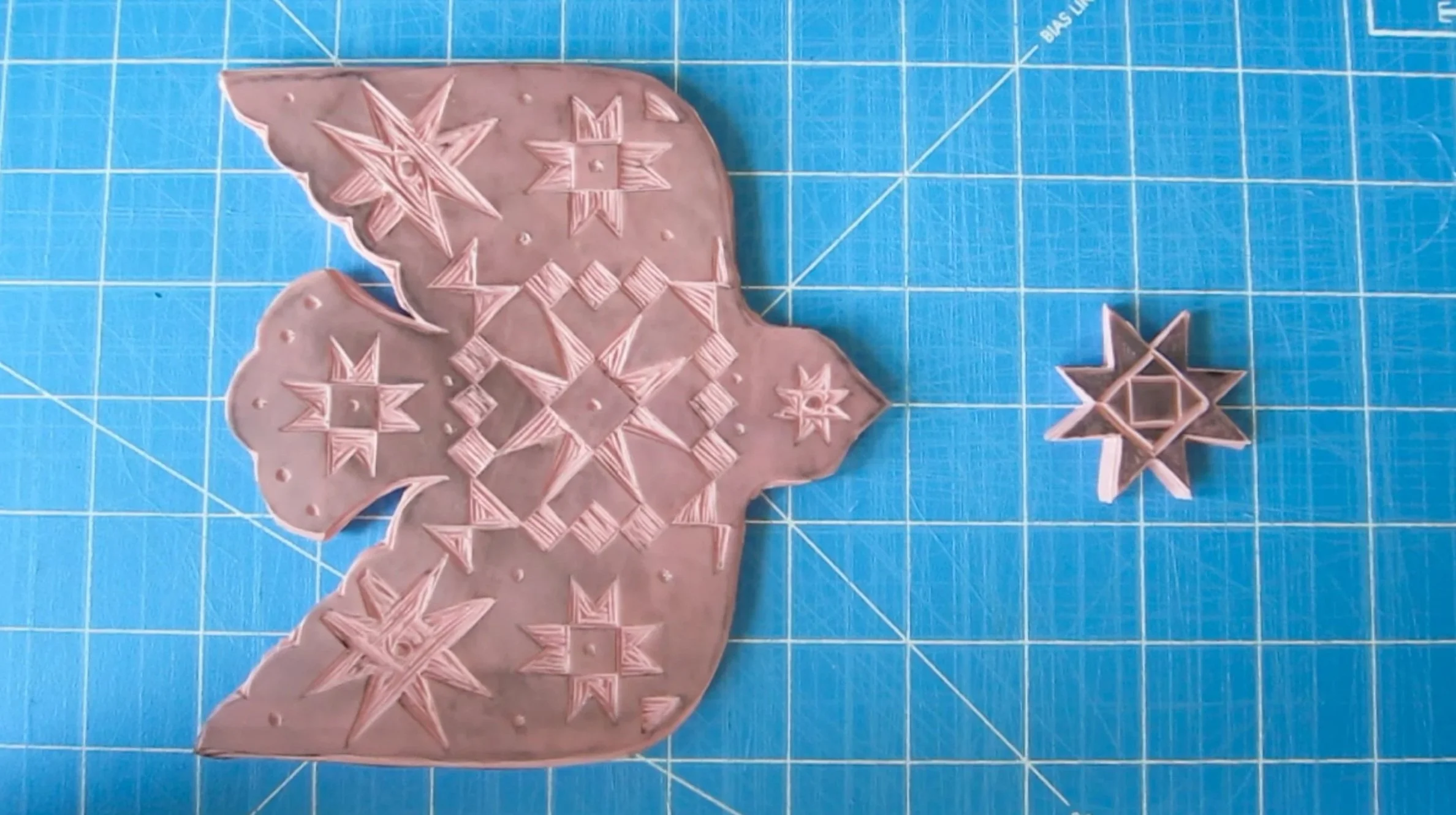 Pink fondant or cookie with intricate star-shaped and geometric cutouts, laid on a blue cutting mat.