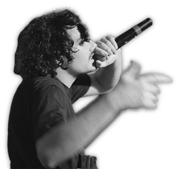 A young person with curly hair singing into a microphone with right arm extended.