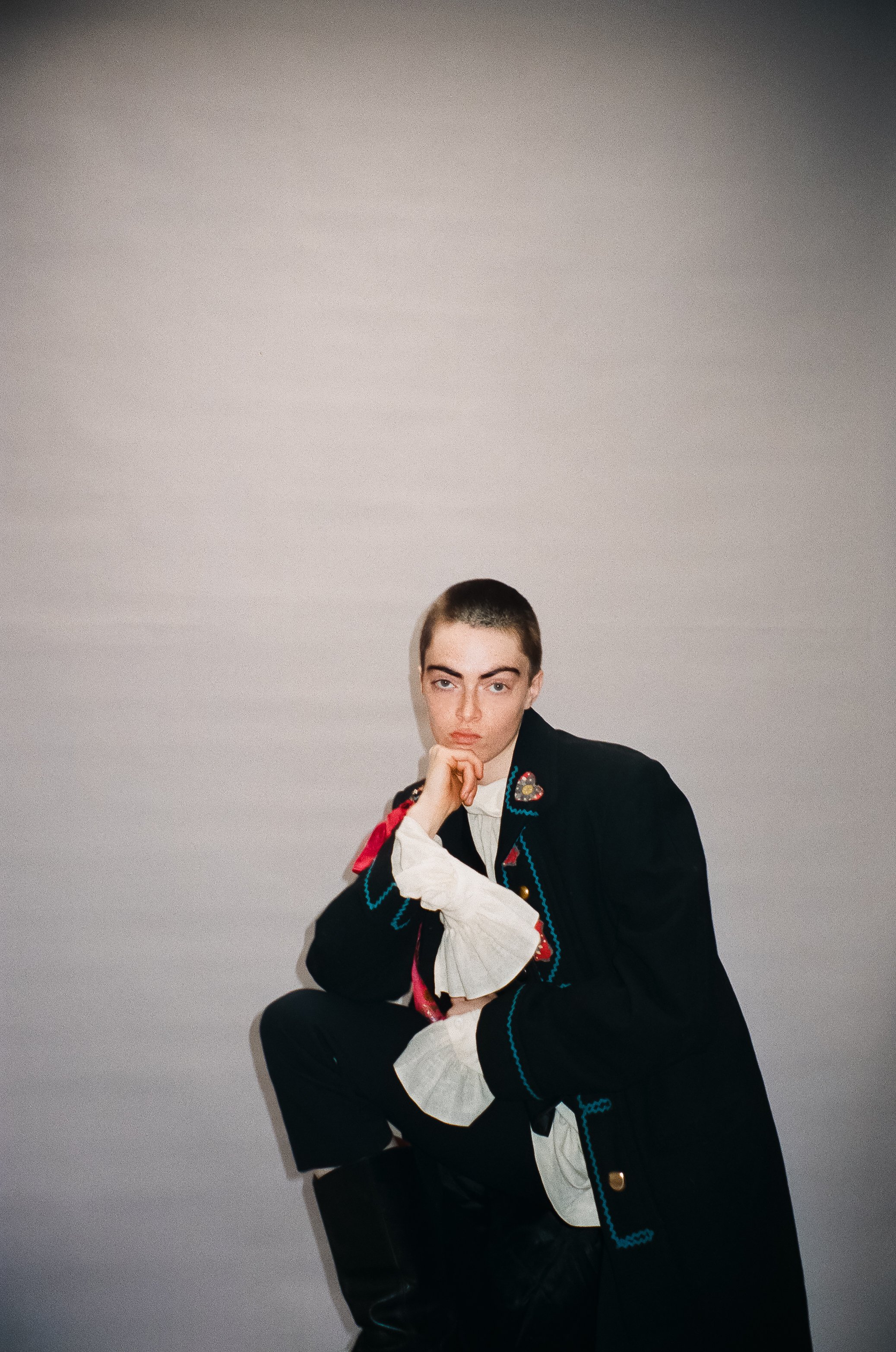 Shane Stevens, high fashion runway model, smiles slyly wearing Jonathan Anderson for Dior-inspired antique coat as she poses for a portrait film photograph taken by NYC fashion photographer Indie Studios on a white seamless backdrop.