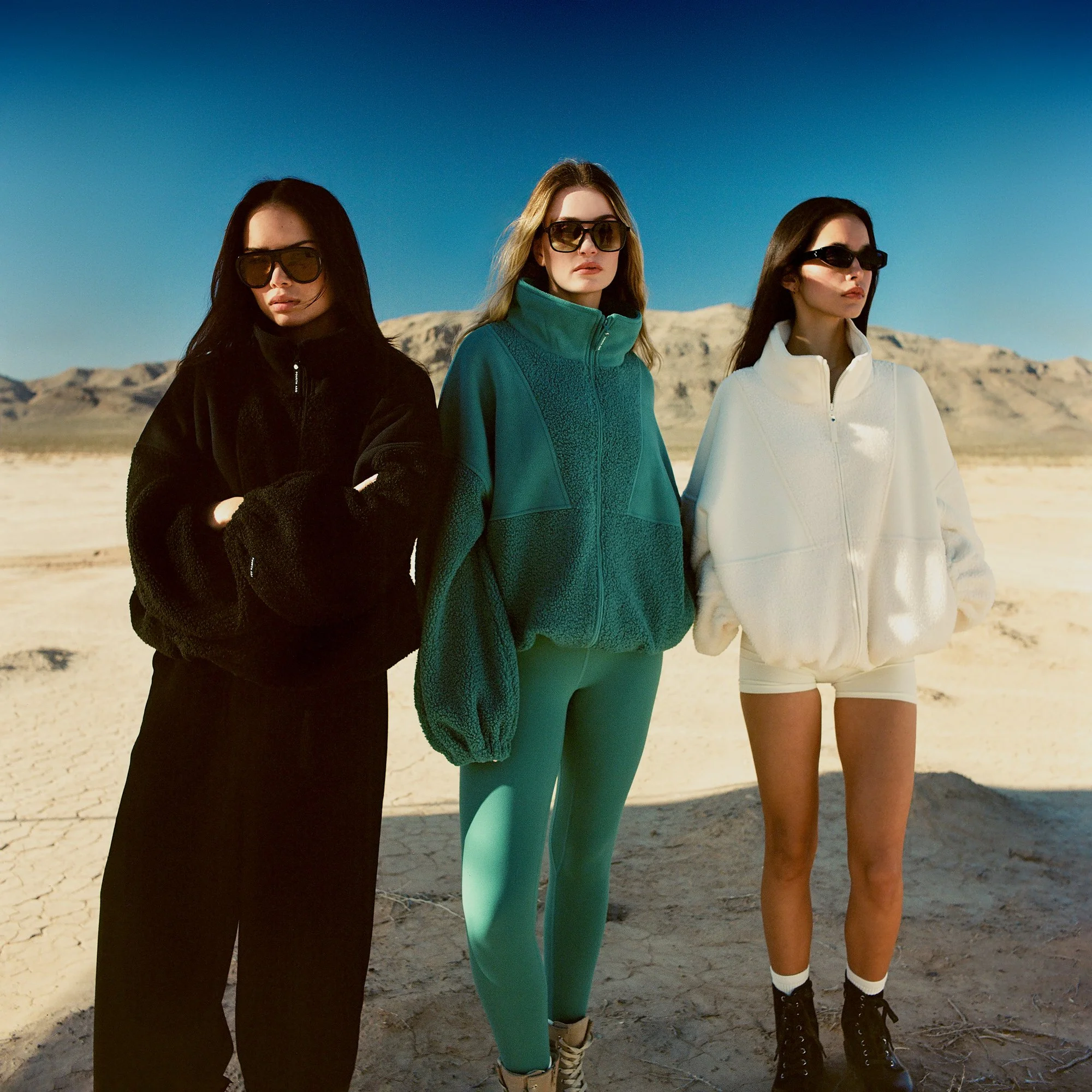 Three fashion models standing in a dry lake bed in the Mojave Desert for a fashion campaign photo and film shoot directed by revolutionary fashion photographer indie studios.  Indie studios produces and directs on-location fashion photography shoots.