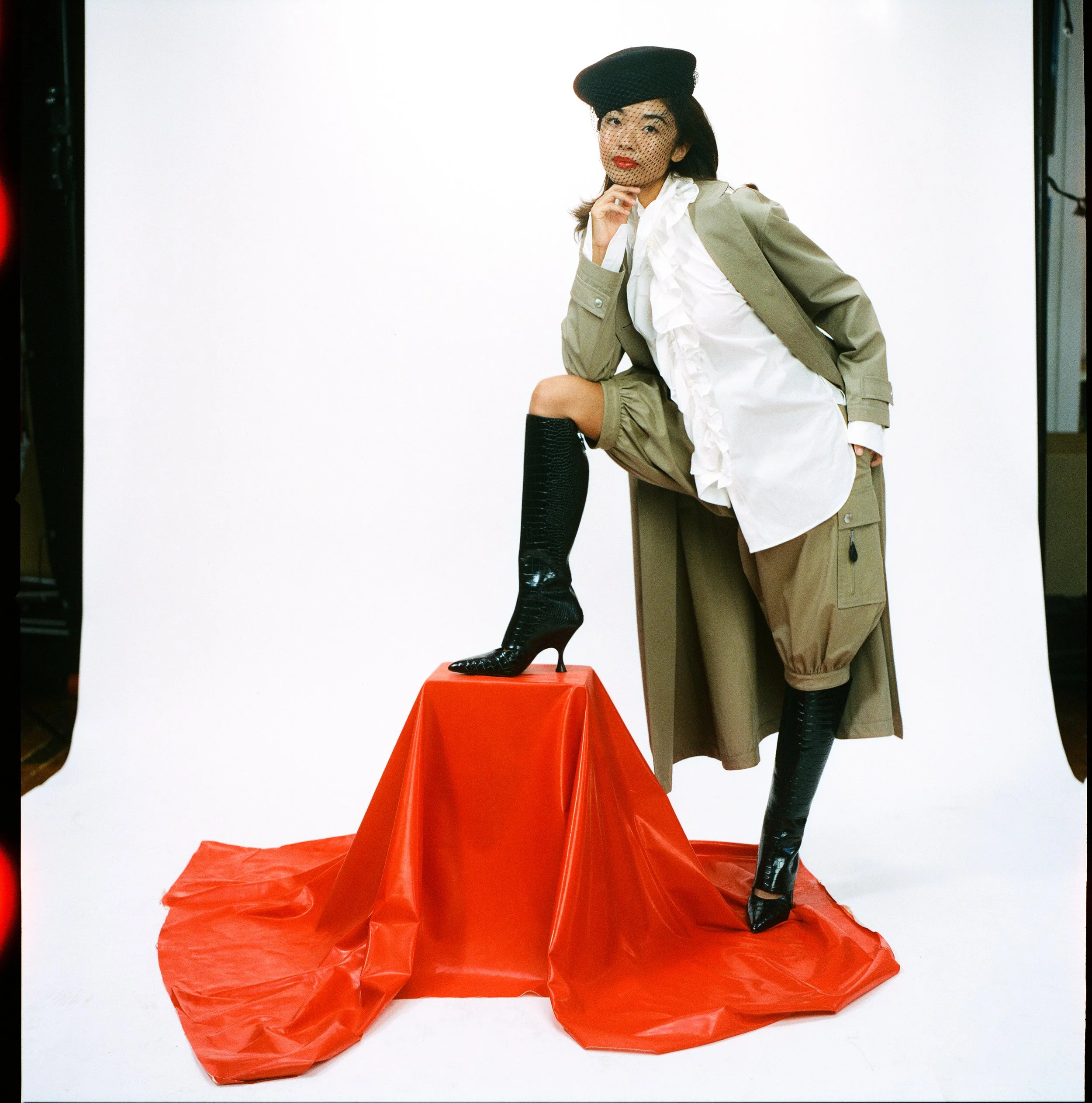 American Ballet Theater dancer Kayla Mak at Indie studios wearing a full look by Christian Dior stands with one leg up in black boots on a red vinyl cube on a white background. Photographed by fashion photographer indie studios on medium format .