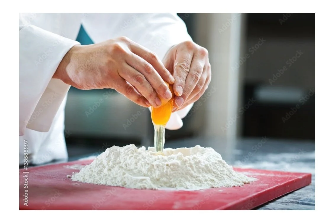 Spin around on a close up of a flour bowl on the cutting board as chef cracks an egg one handed and starts to hand mix the two.