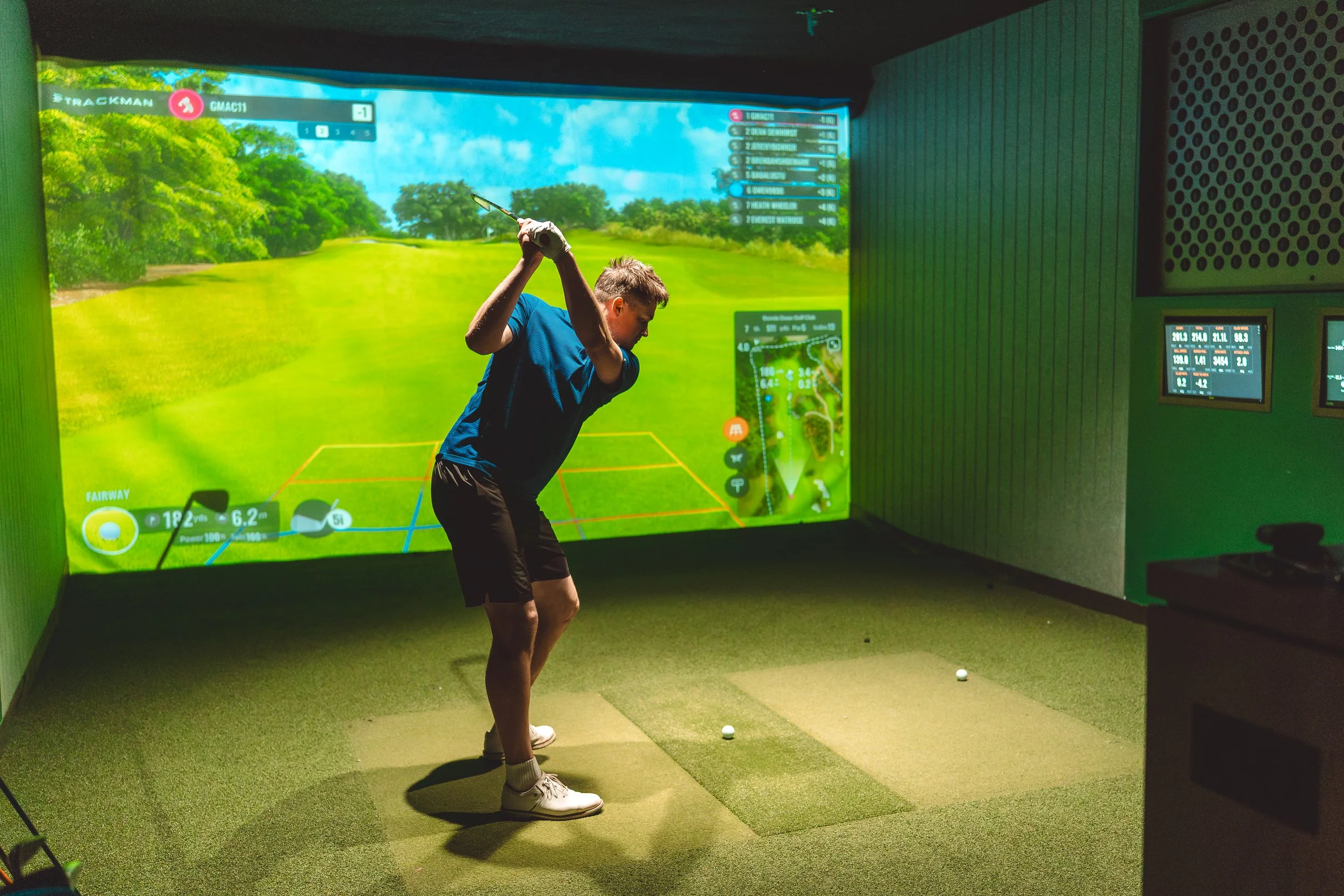 A picture of a man swinging a golf club in an indoor golf simulator