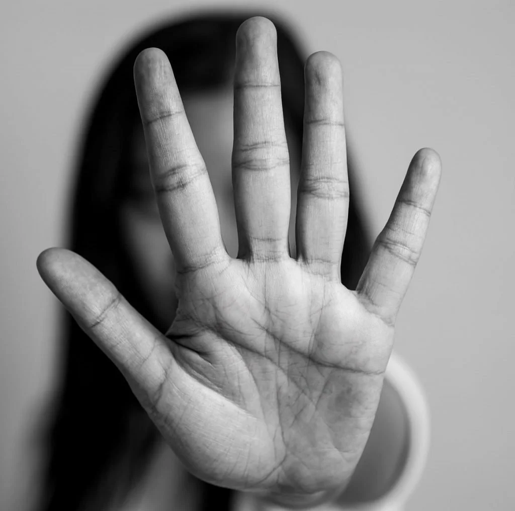A person with dark hair holds up their hand, signaling stop, with fingers spread in front of their face. The image is in black and white.