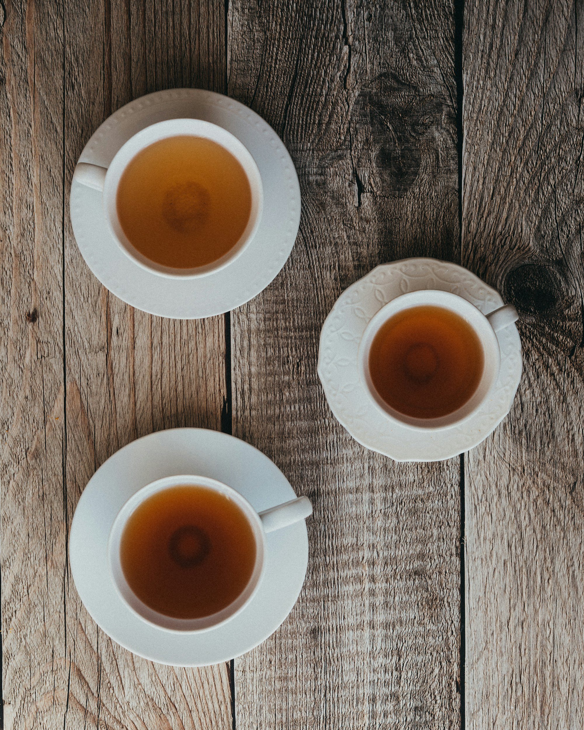 Top-down view of three white teacups filled with tea placed on mating white saucers on a rustic wooden table.
