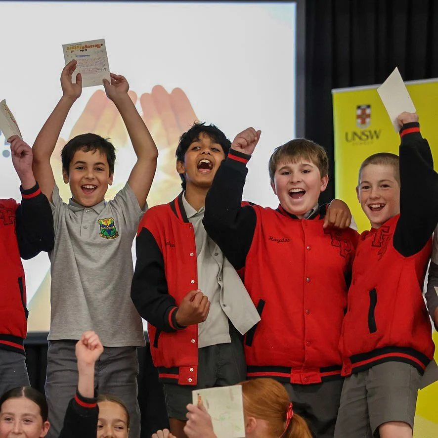 students with happy faces and raised arms in front of signage
