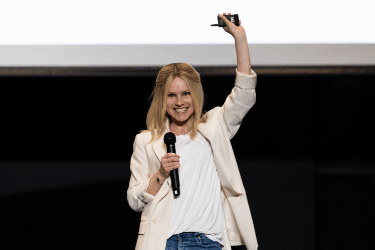 Smiling woman speaking onstage with one arm up