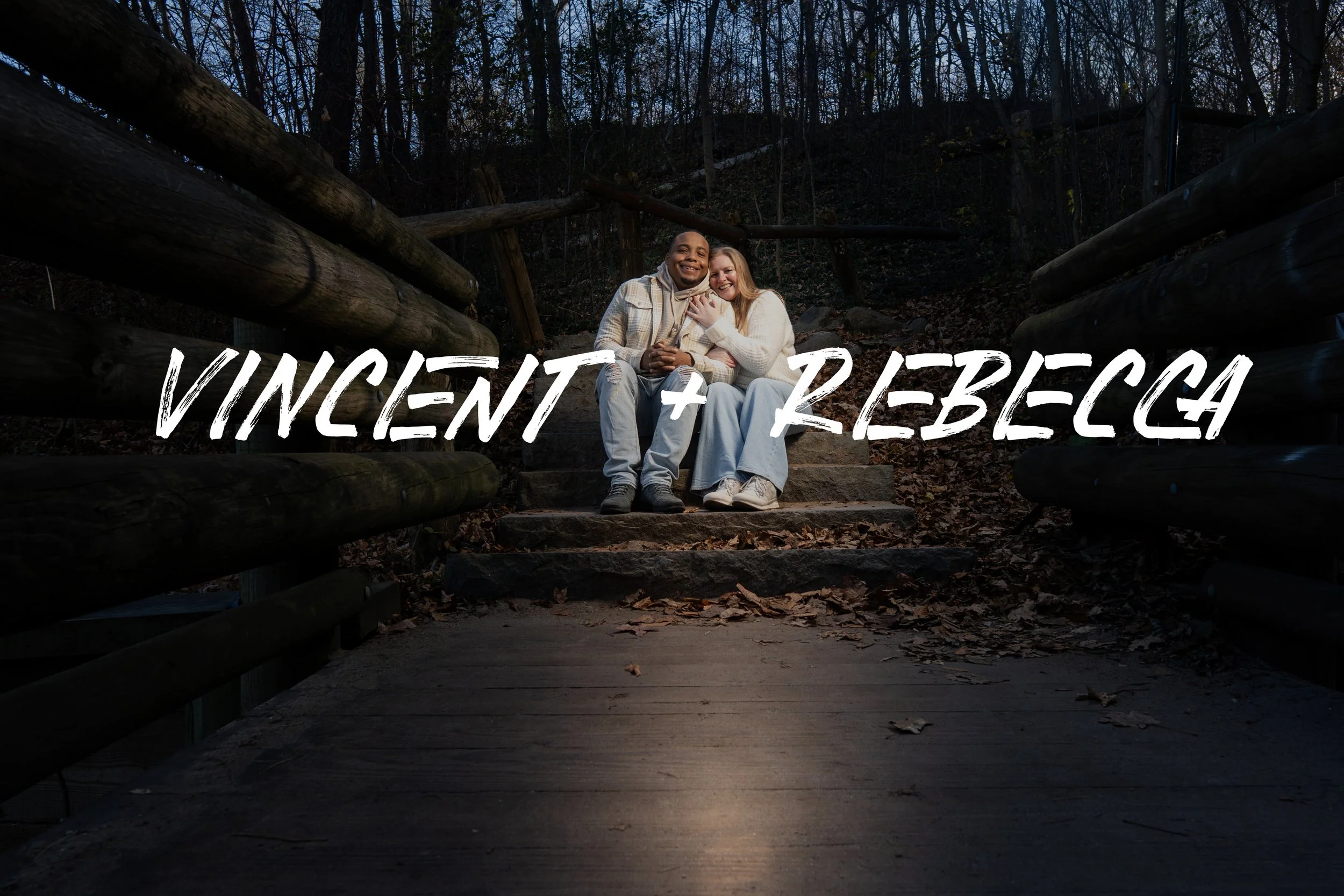A couple sitting on steps in a wooded park at dusk, with the text 'VINCENT + REBECCA' overlaid.