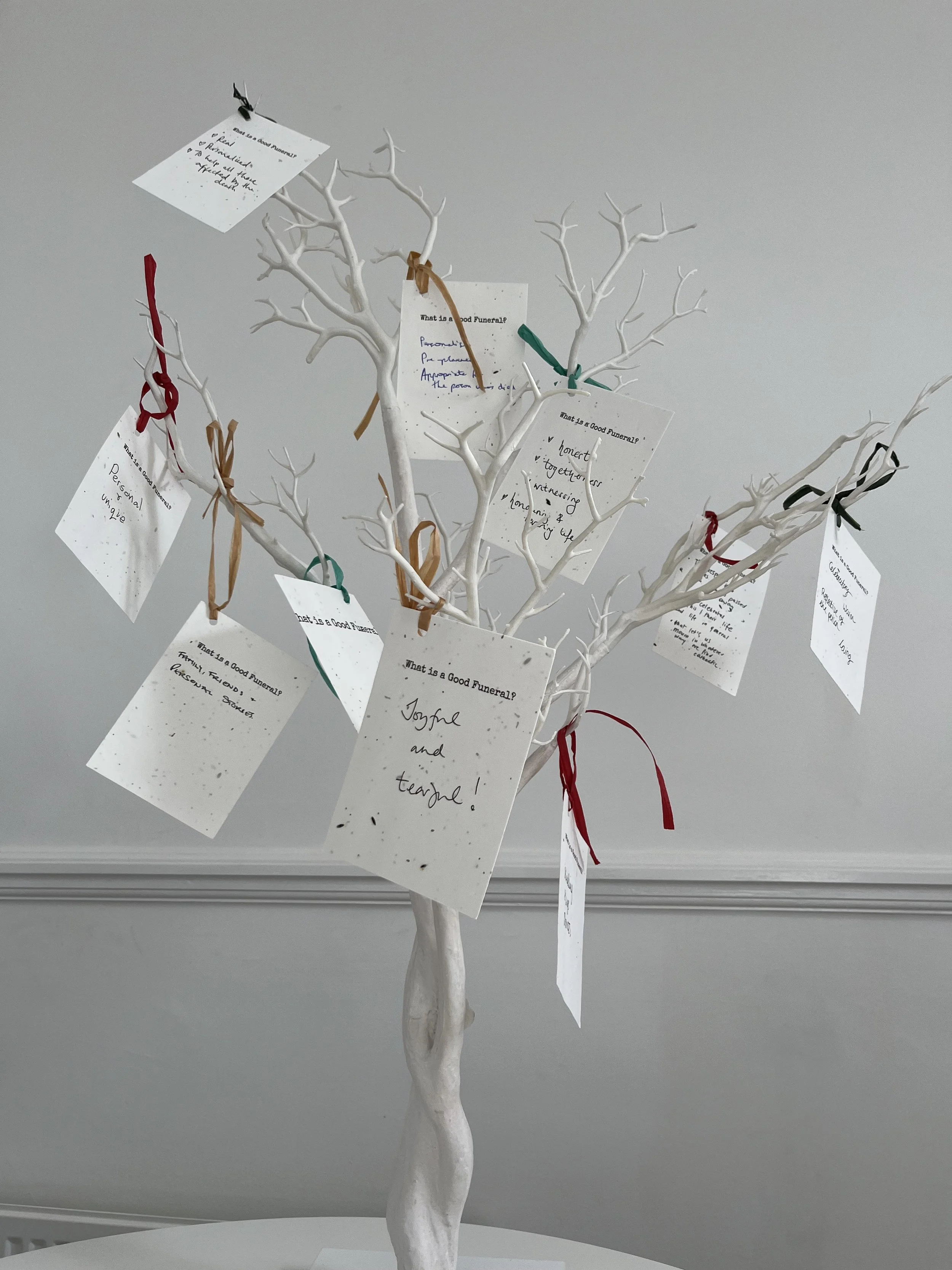 Memory tree in white with nine tags attached,  with handwritten notes on what a good funeral is.