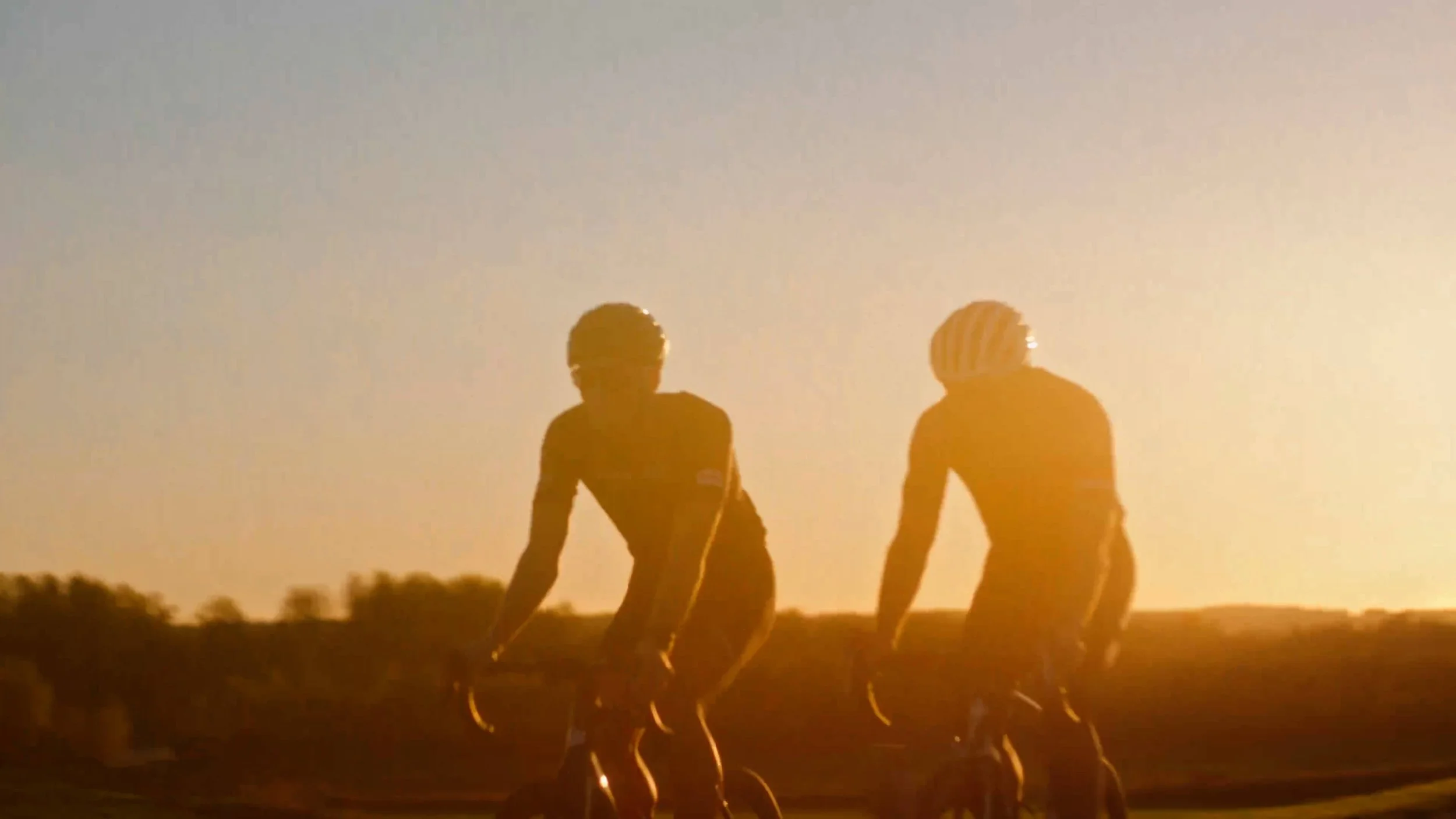 Twee wielrenners fietsen in de zonsondergang op een landweg.