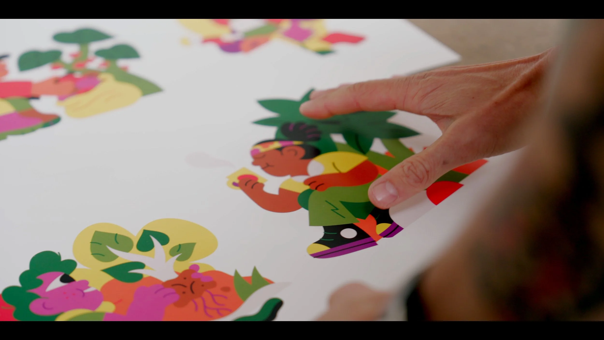 Een hand plaatst een gekleurd papieren stukje op een grote collage van andere kleurrijke papieren kunstwerken.