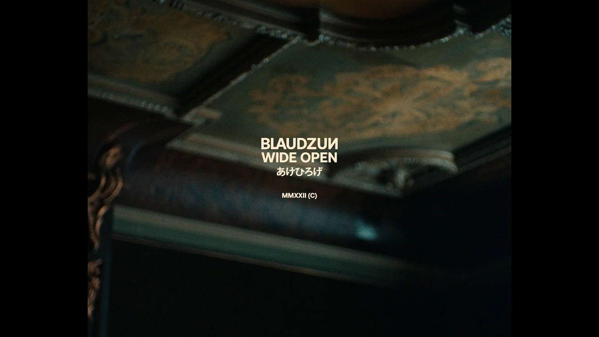 Close-up van een meubelstuk met gedetailleerde houtbewerking en tekst die zegt "BLAUDZUIN WIDE OPEN", met Japanse karakters en het jaartal MMXXII (2022) in het midden.