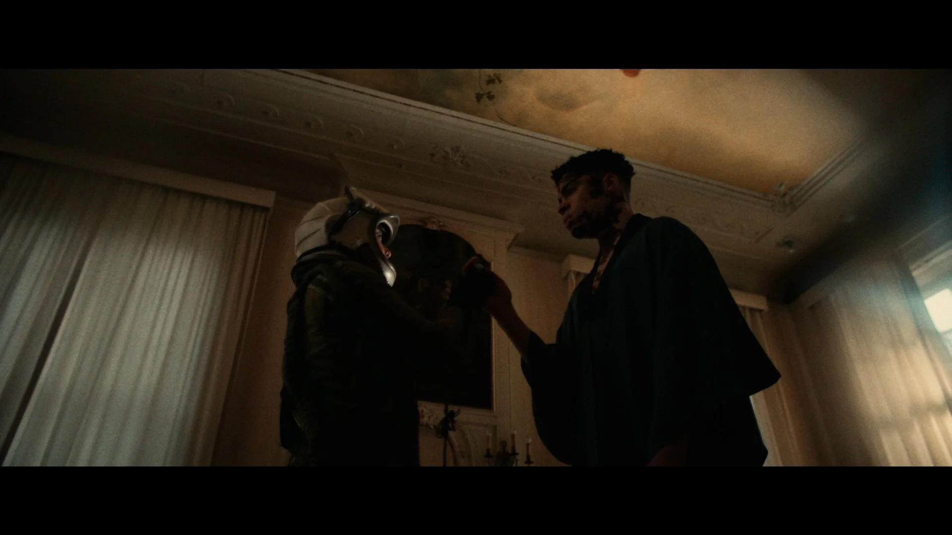 Twee jonge mannen in een kamer, één met een drone op zijn hoofd en een gelaatbescherming, de ander in zwarte kleding, staat tegenover elkaar.