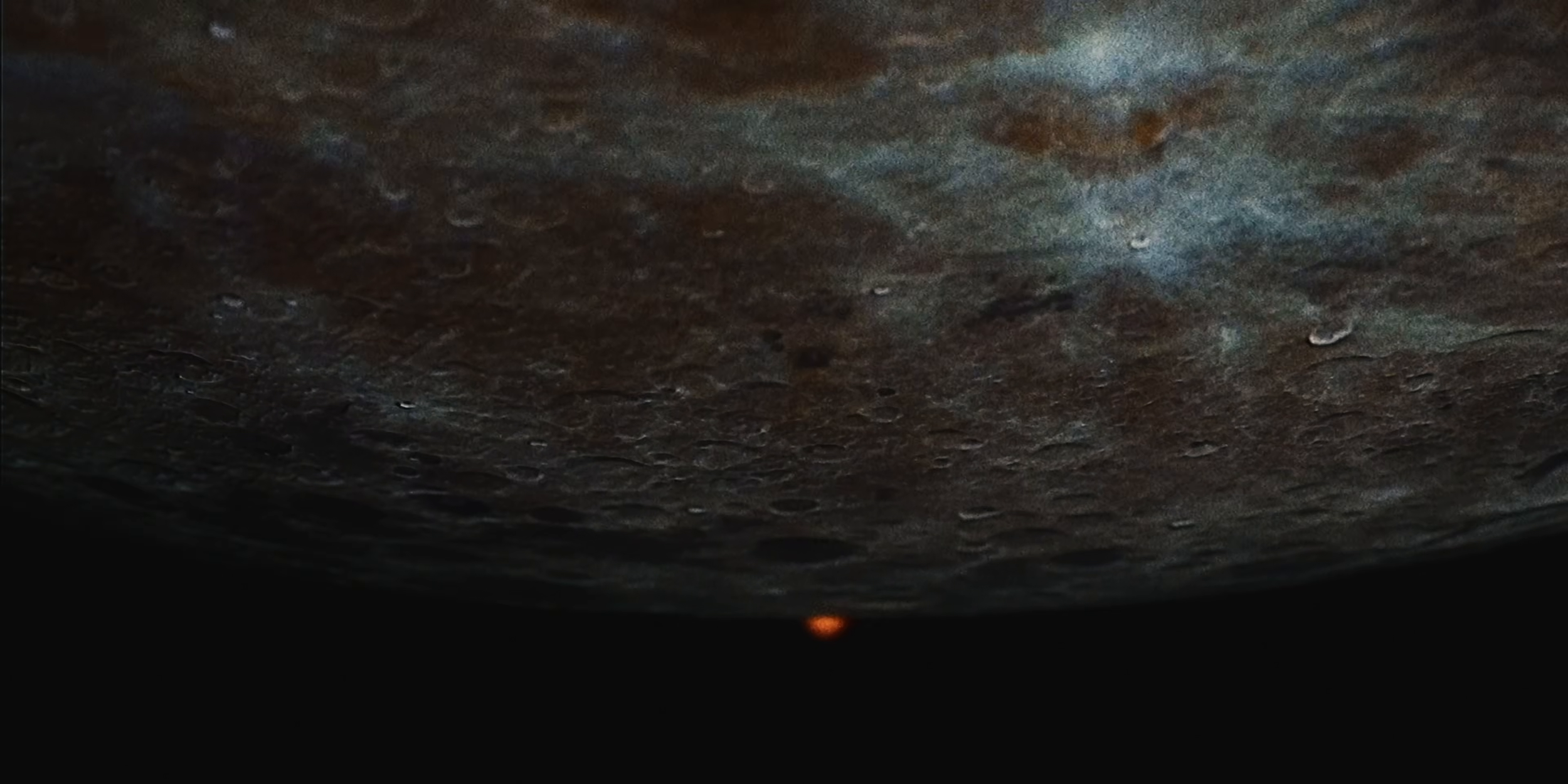 Close-up van een donkere, gladde, wellicht metalen of stenen ondergrond met enkele kleine reflecterende oppervlakken en een oranje vlek onderaan.