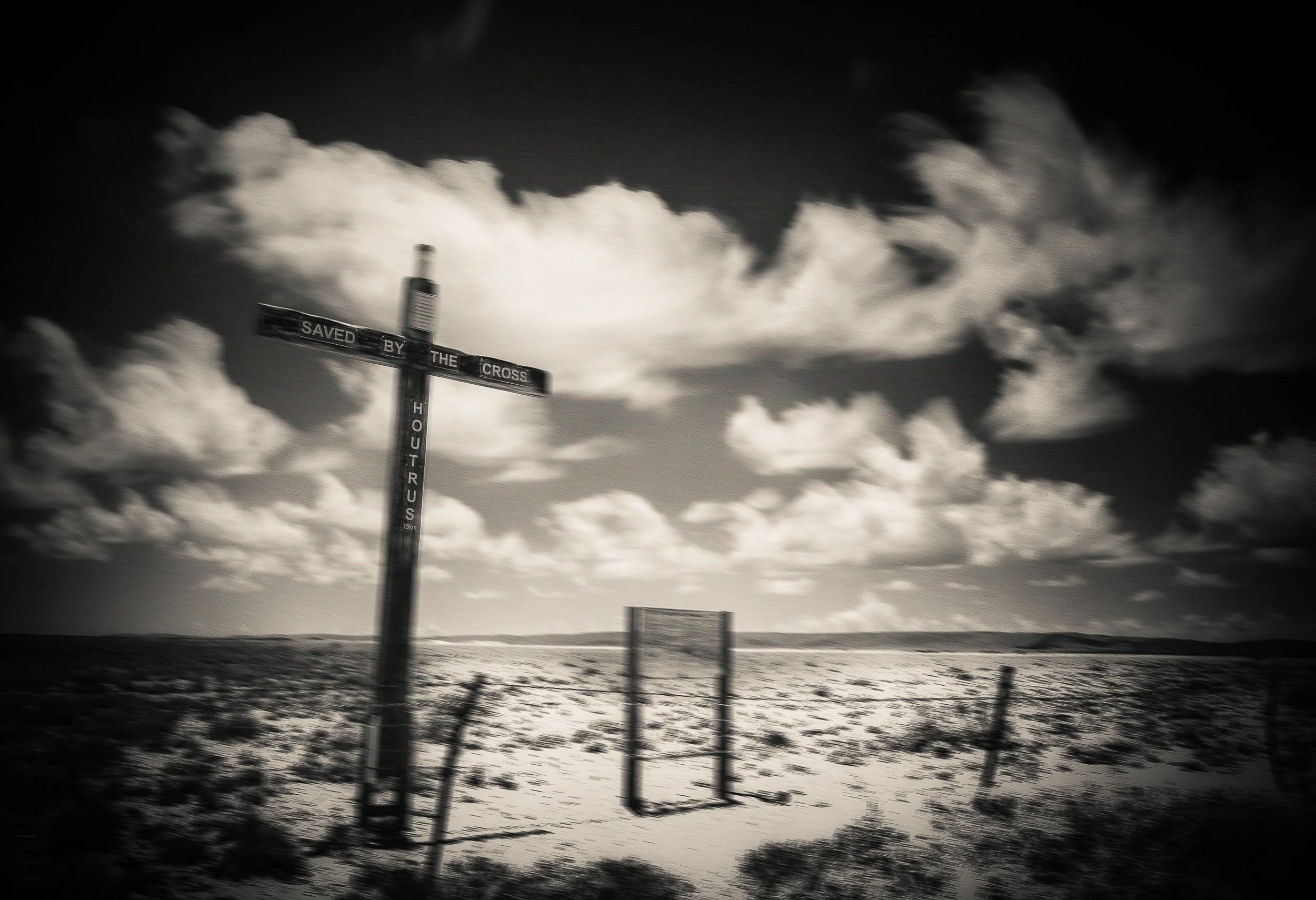 Black and white long exposure landscape with clouds moving around a wooden cross in an open rural landscape, 242-second exposure.