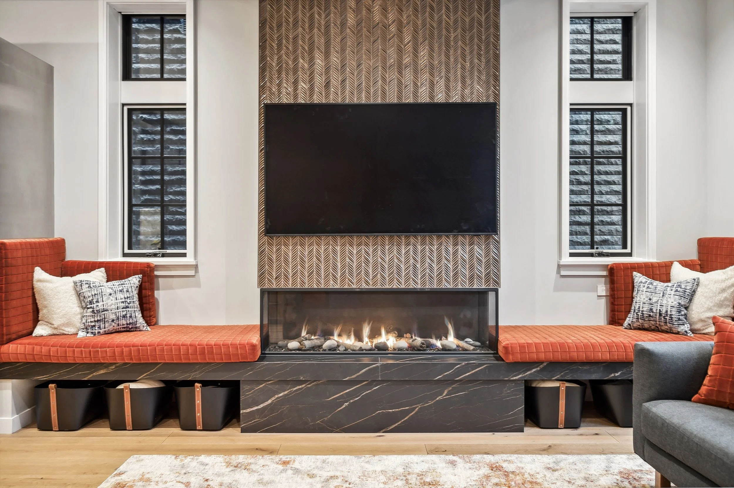Modern linear gas fireplace with a black marble hearth featuring built-in orange velvet bench seating and under-bench storage bins.