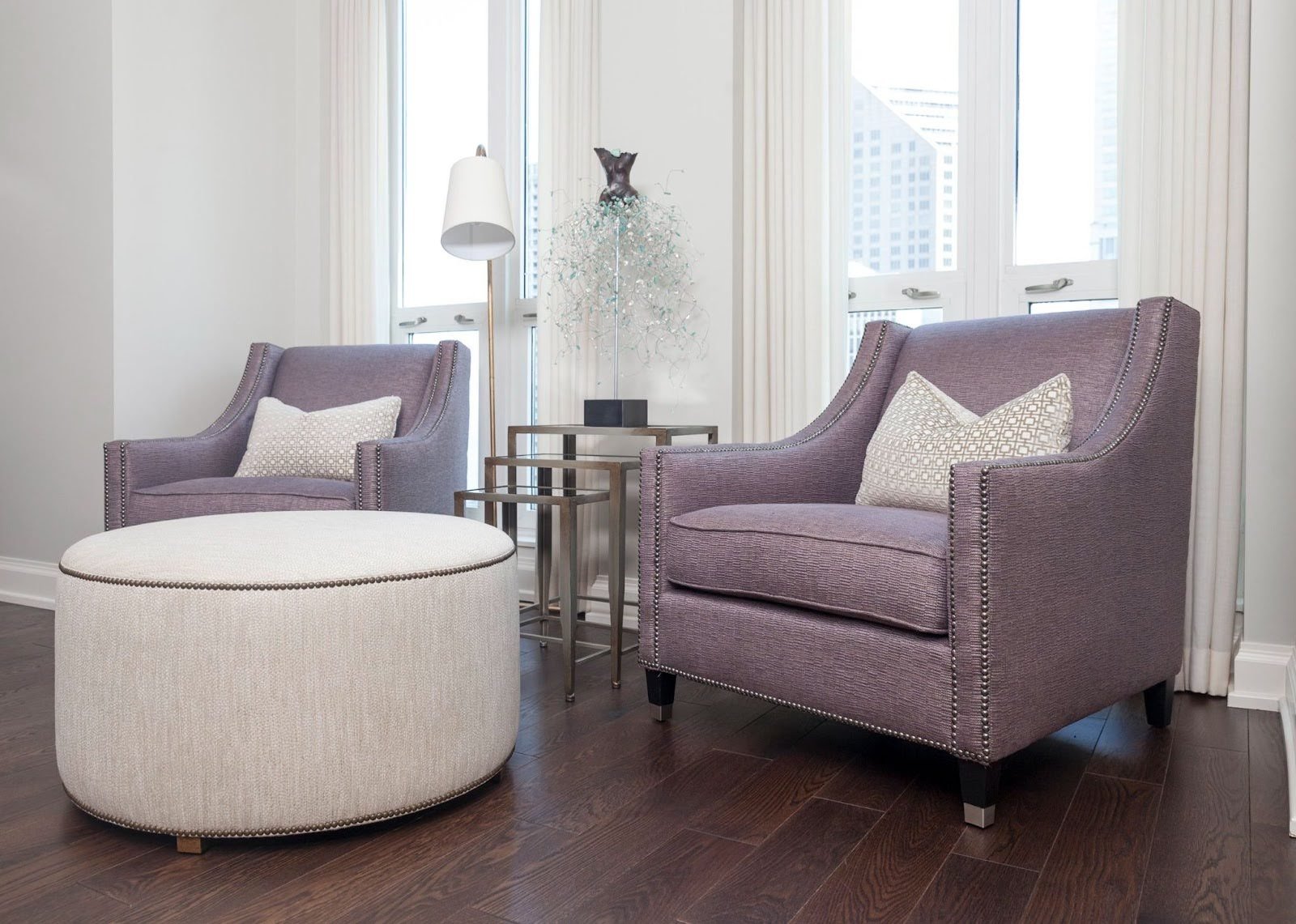 Regal lavender textured accent chairs with silver nailhead trim, a large cream round ottoman, and tiered metal side tables at the Waldorf Astoria Project