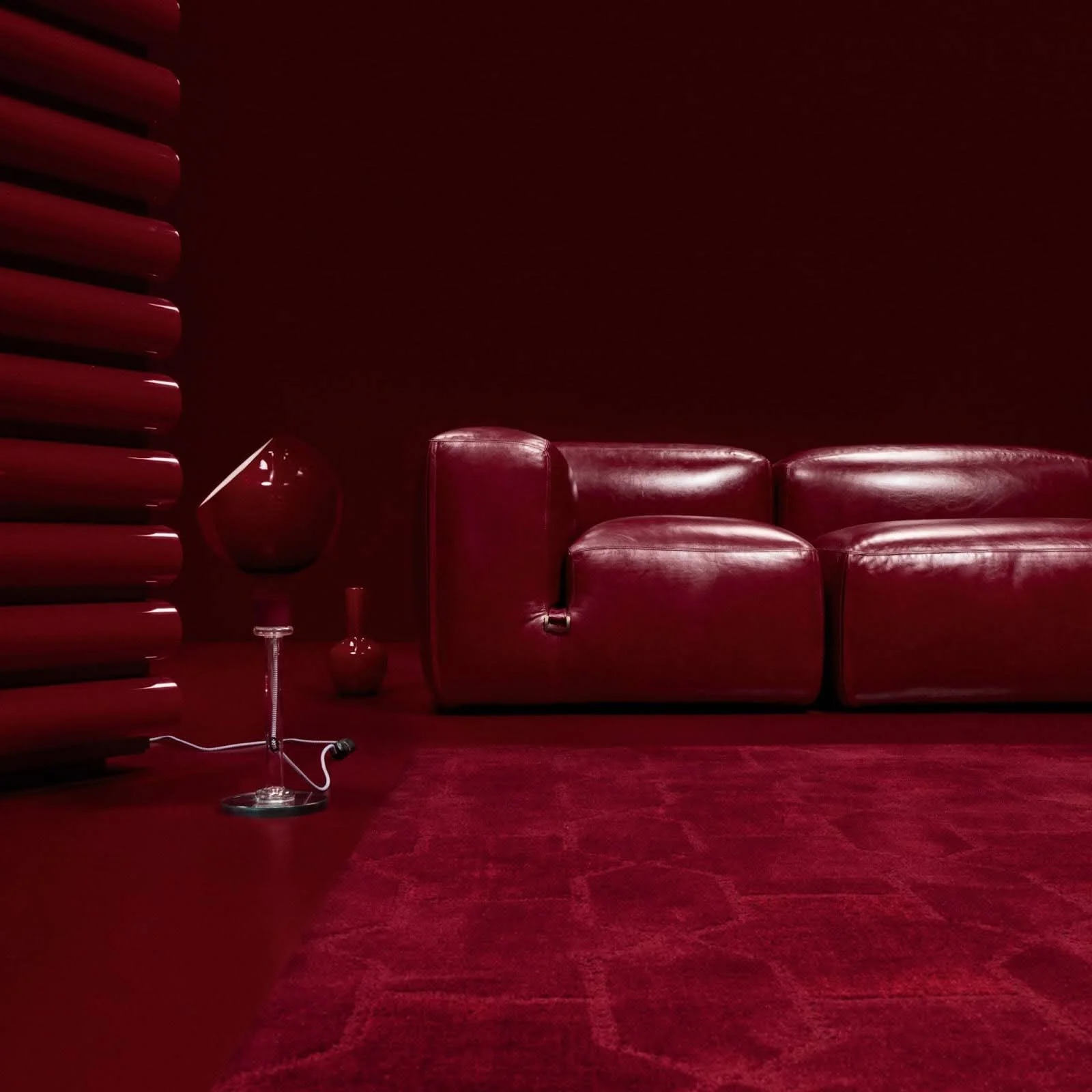 A bold monochromatic living room featuring a deep red leather sofa, a red circular lamp, and a textured red rug, showcasing the unexpected red theory trend