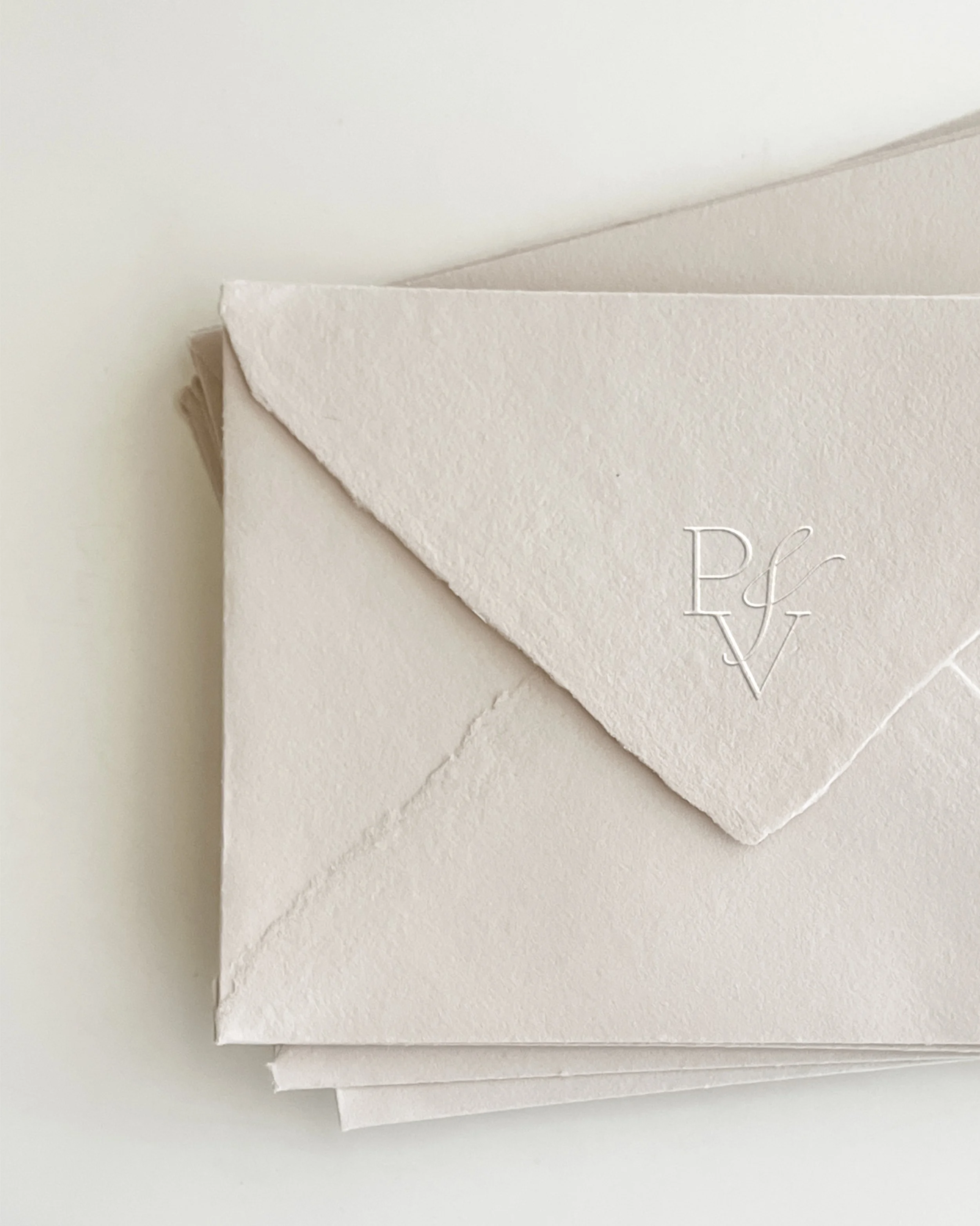Close-up of stacked white textured paper envelopes, one with an embossed monogram with the letters P, V, and F.