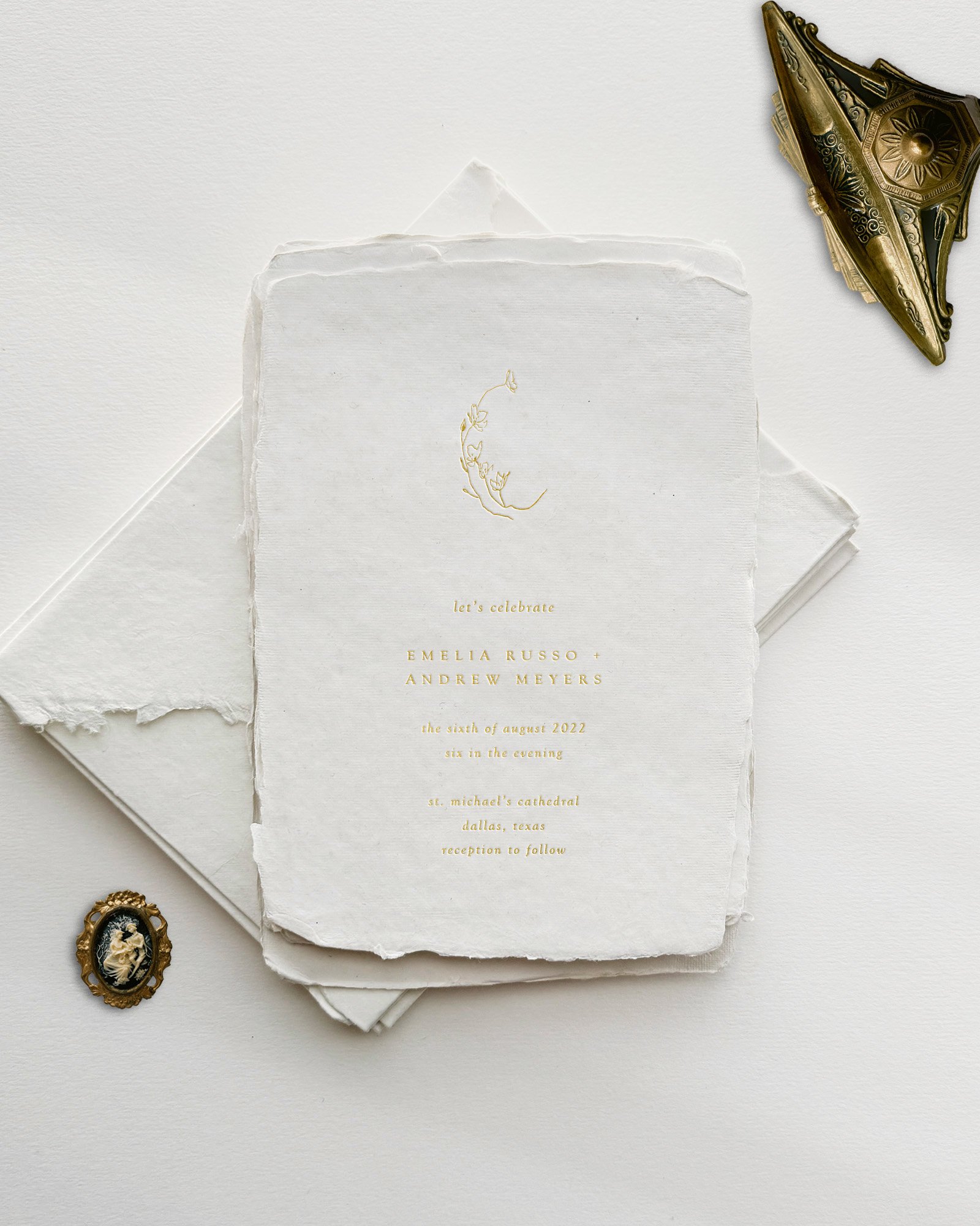 Wedding invitation card with gold foil text, surrounded by vintage jewelry items on a white textured background.