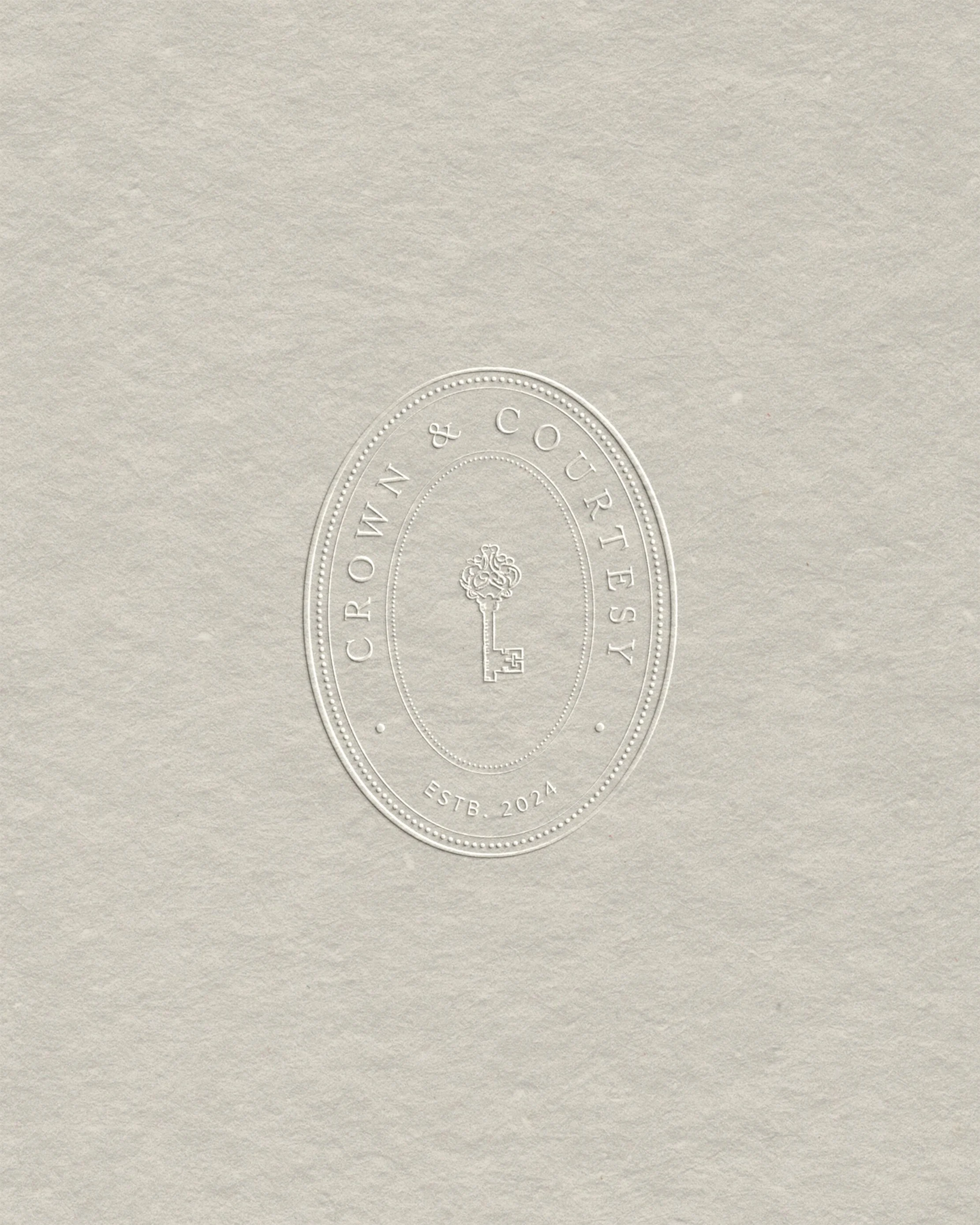 Embossed logo on beige paper with the text 'Crown & Courtesy' and 'ESTB. 2024' surrounding a key with a floral top.