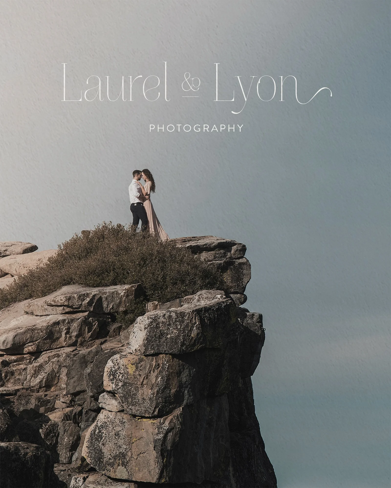 A couple dressed in formal attire standing on rocks at the edge of a cliff, with the sky in the background. The text overlay says 'Laurel & Lyon Photography'.