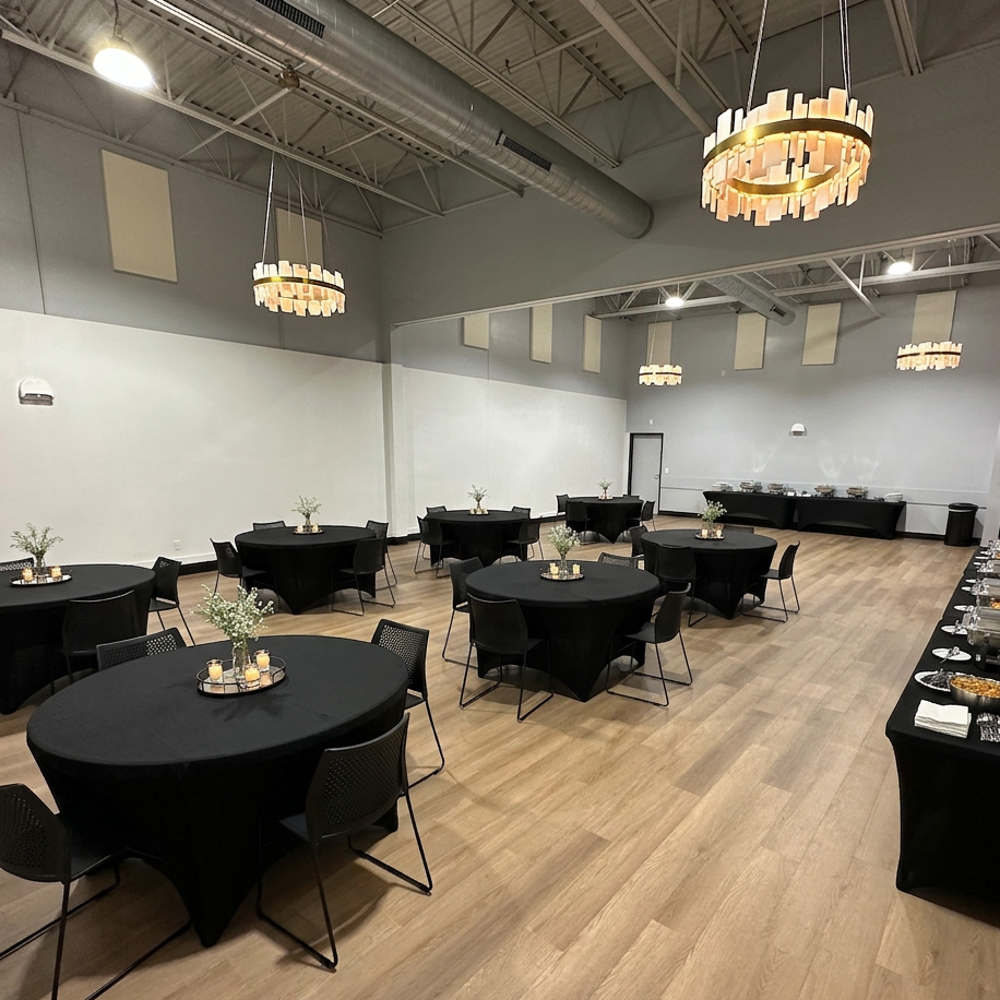 Modern, carpeted interior of The Falls event space featuring dark ceiling fixtures and round tables arranged for a boutique gathering.