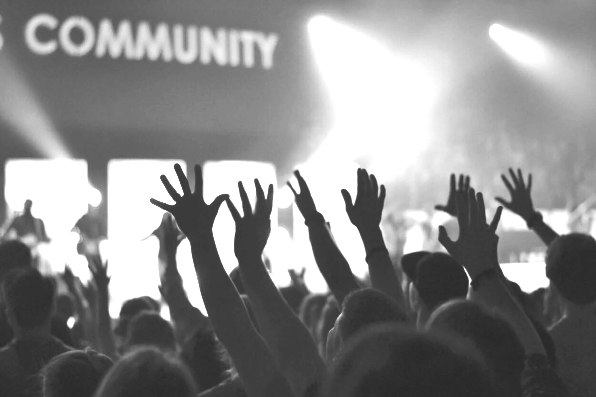 Silhouettes of a crowd with raised hands at a concert or live community event.