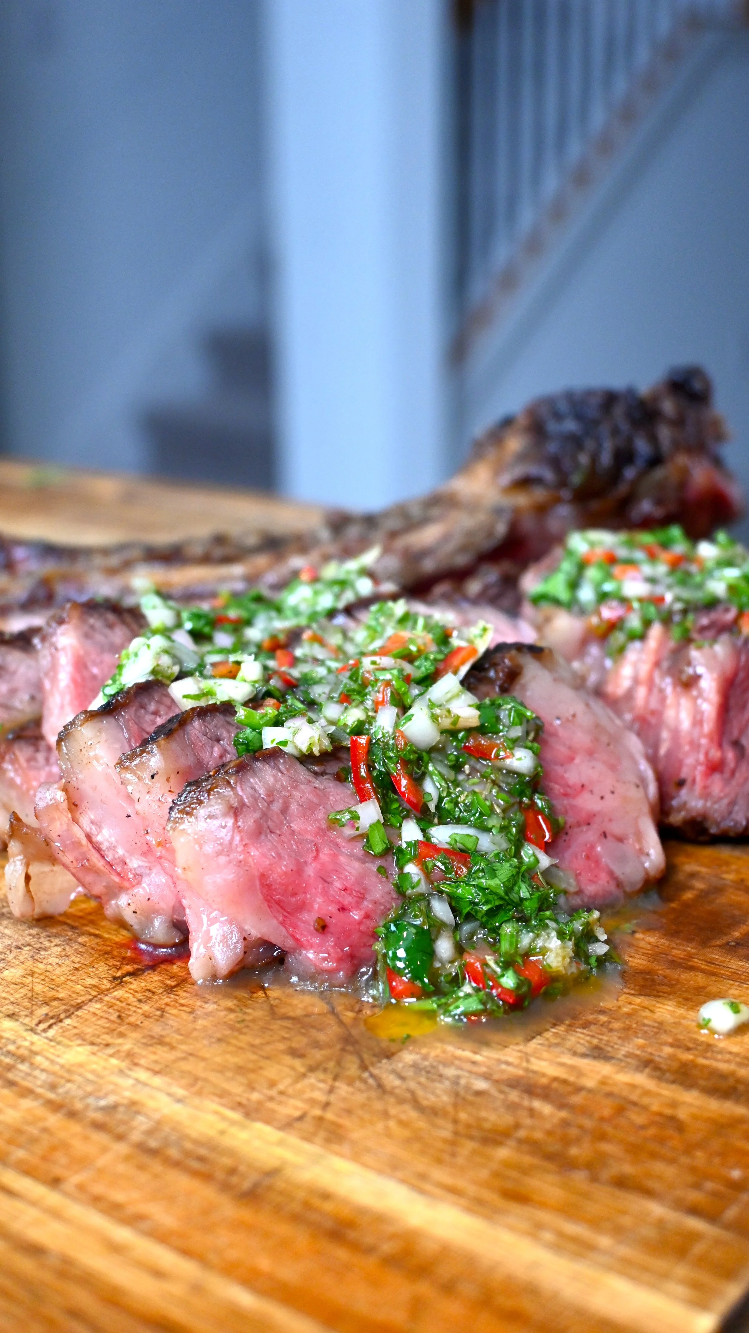 Slices of cooked beef topped with chopped green onions, red chili peppers, and herbs on a wooden cutting board.