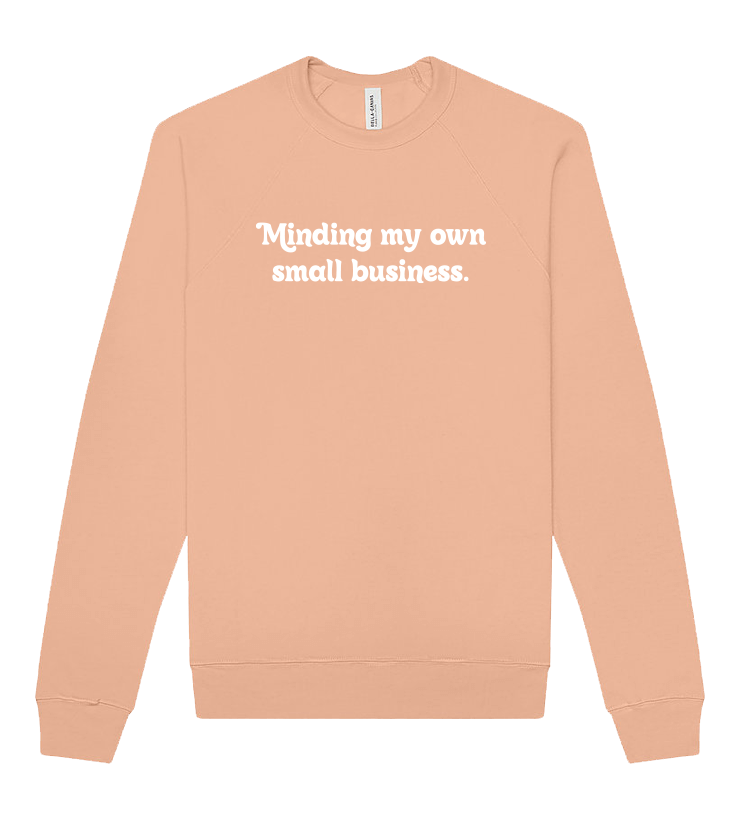 A peach-colored sweatshirt with the phrase "Minding my own small business." written in white text on the front.