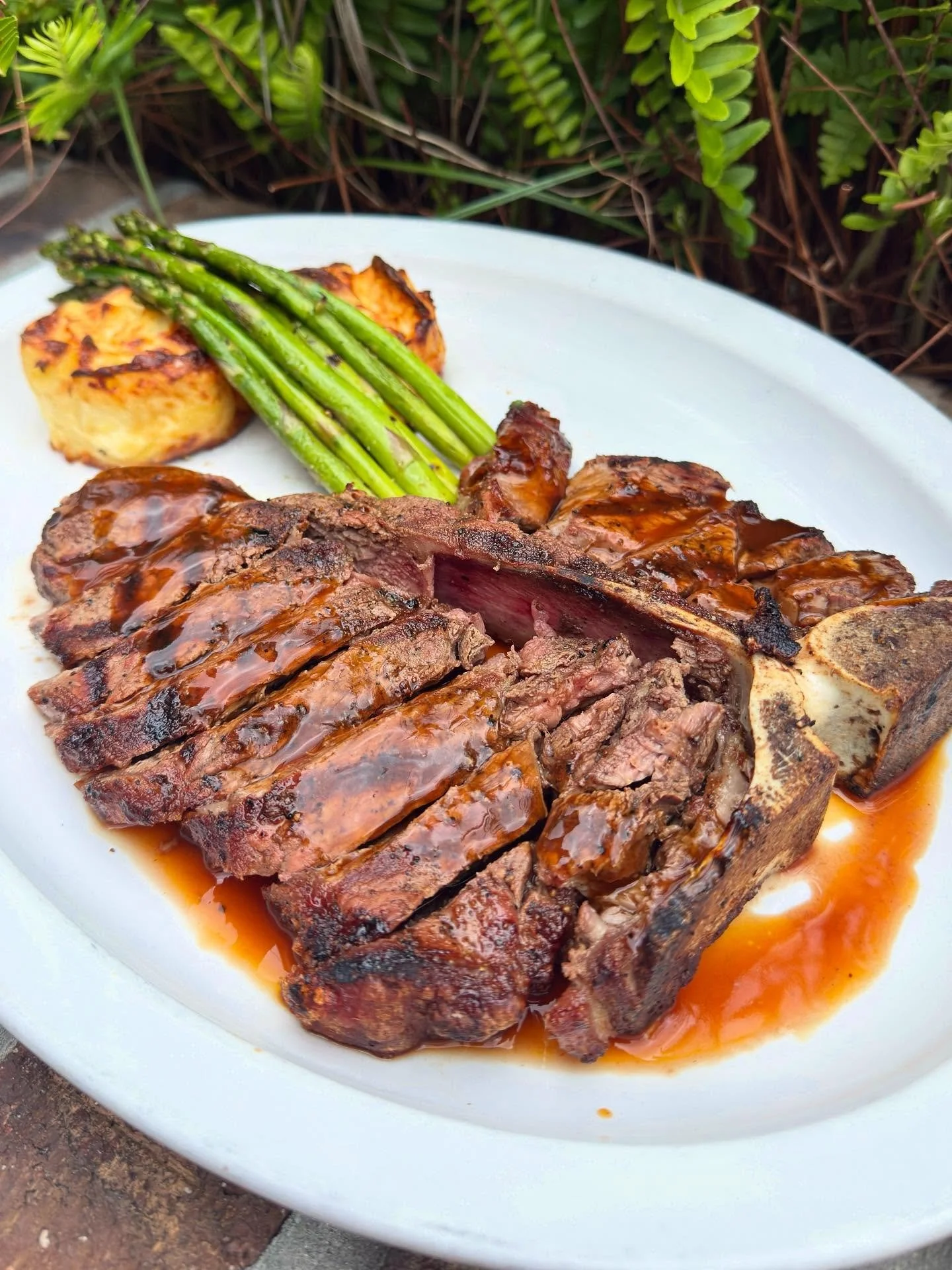 Steak with grilled asparagus, potato cakes, and gravy on a white plate