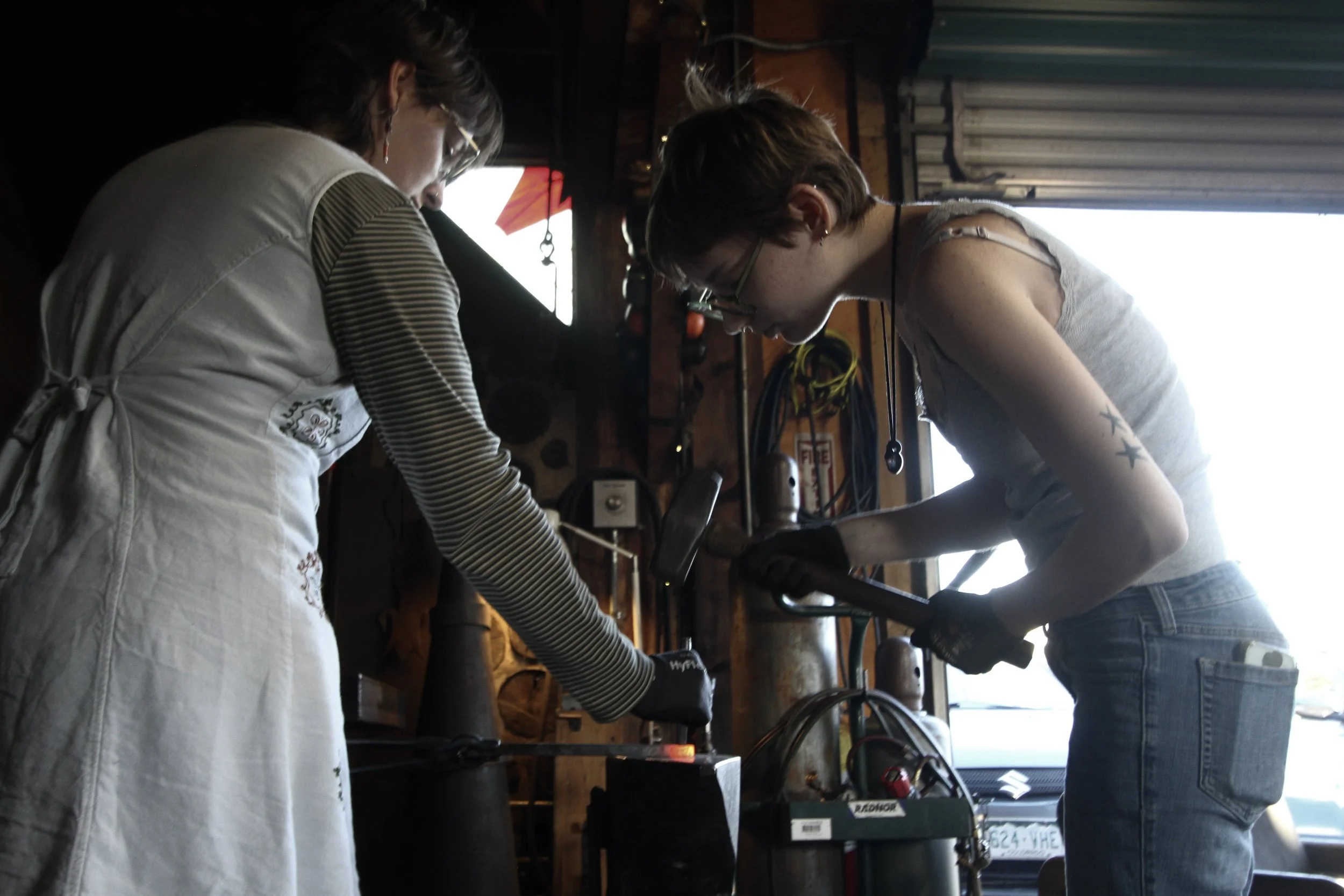  Crew member  August Duncan  and second-year student  Merritt Yoder  punch metal on an anvil during open forge hours on Nov. 4, 2025, in Swannanoa, N.C. (Echo/Vivian Bryan) 