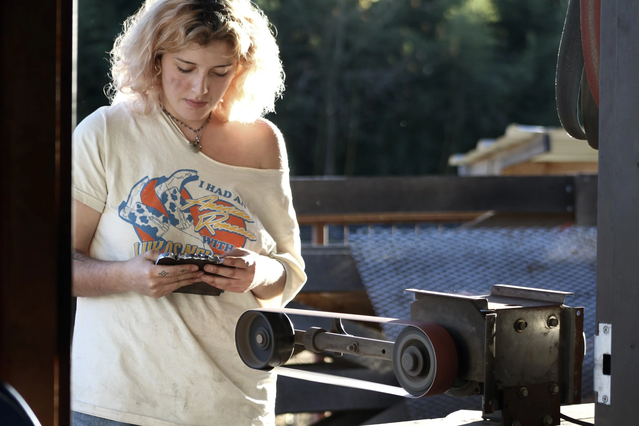  Sophomore  El Ferrara  works a piece of metal on the belt sander outside the forge on Nov. 4, 2025, in Swannanoa, N.C. (Echo/Vivian Bryan) 