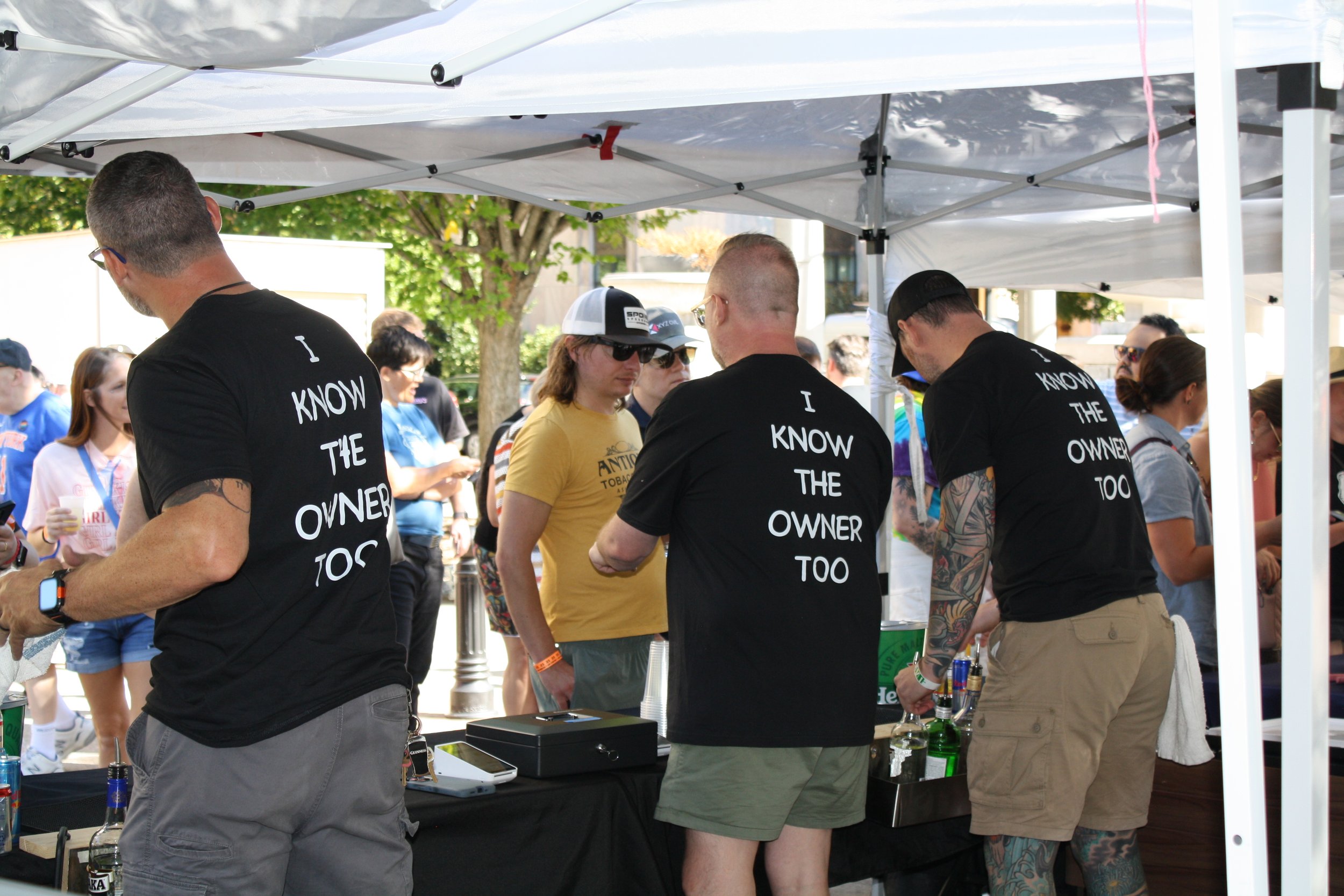 Workers at a pop up bar tent all sport matching shirts reading “I Know the Owner” at Blue Ridge Pride on Sep. 26, 2026 in Pack Square Park in Asheville, N.C. (Echo/Emma Taylor McCallum) 