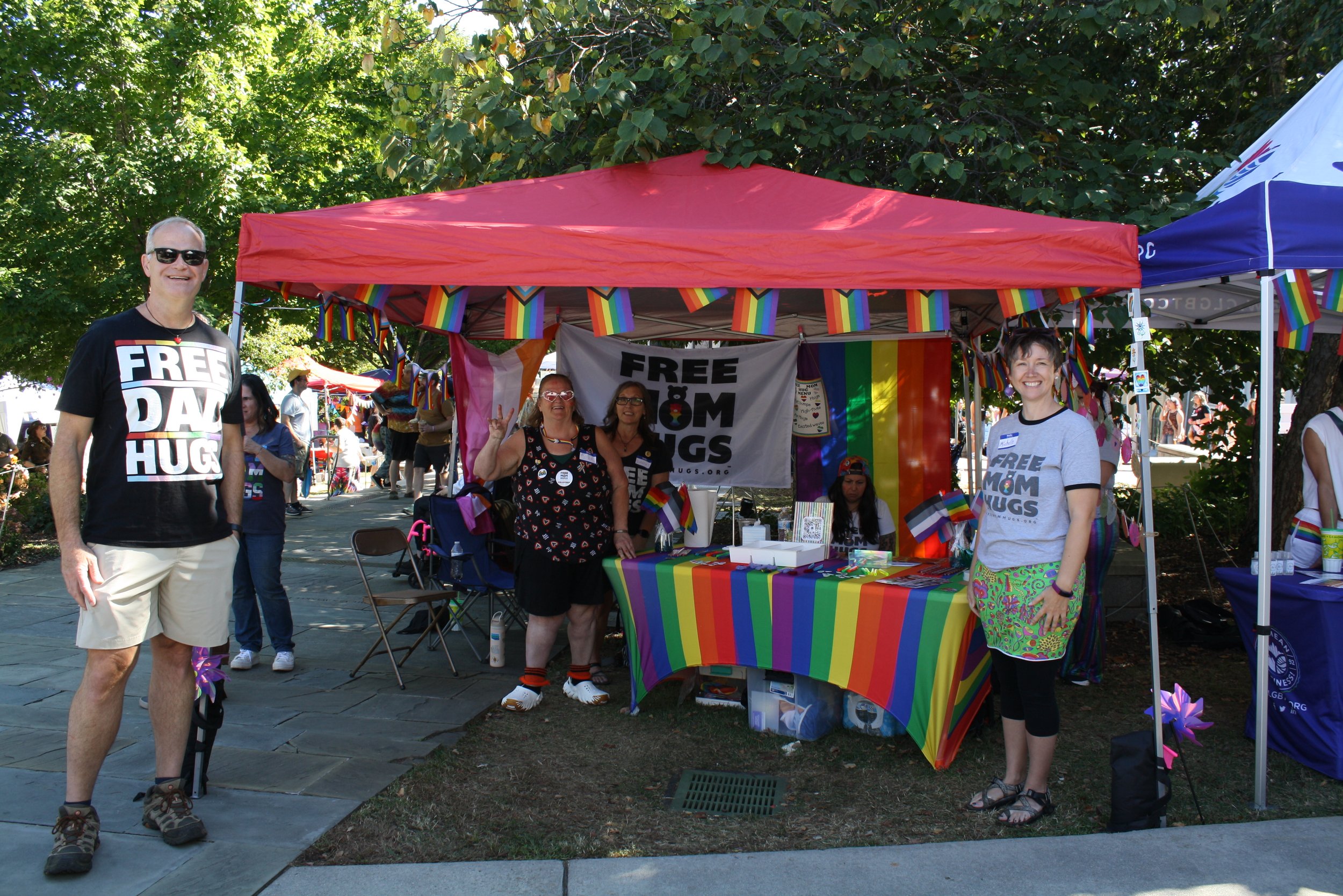  Volunteers gathered around a tent wearing shirts reading “ Free Mom Hugs” and “Free Dad Hugs” at Blue Ridge Pride on Sep. 26, 2026 in Pack Square Park in Asheville, N.C. (Echo/Emma Taylor McCallum) 