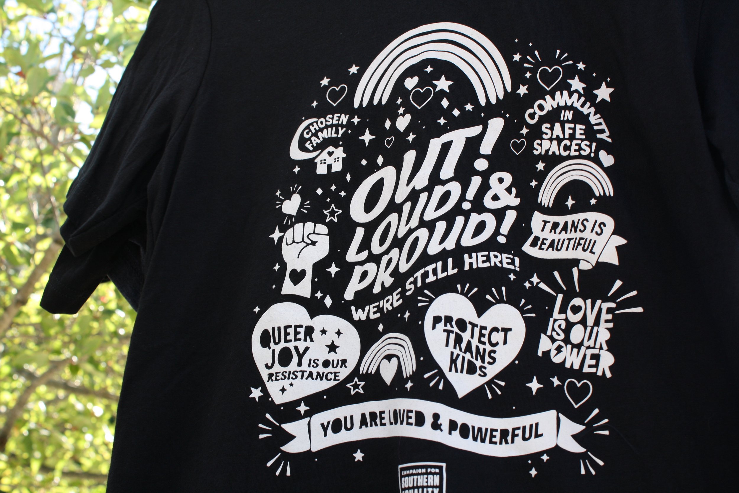  A shirt reading “Out Loud and Proud, We’re Still Here” at the Campaign for&nbsp; Southern Equality table at Blue Ridge Pride on Sep. 26, 2026. Asheville, N.C. (Echo/Emma Taylor McCallum) 