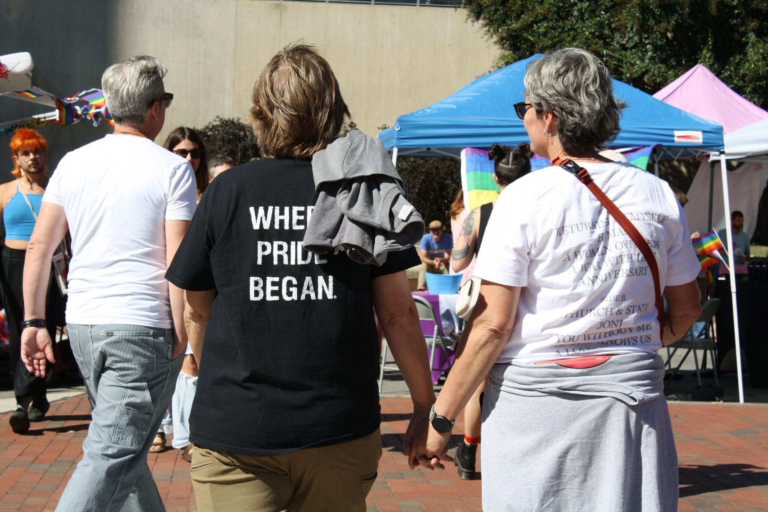 Two attendees of the Blue Ridge Pride hold hands as they walk through the festival. On wears a shirt reading “When Pride Began” on Sep. 26, 2026 in Pack Square Park in Asheville, N.C. (Echo/Emma Taylor McCallum) 