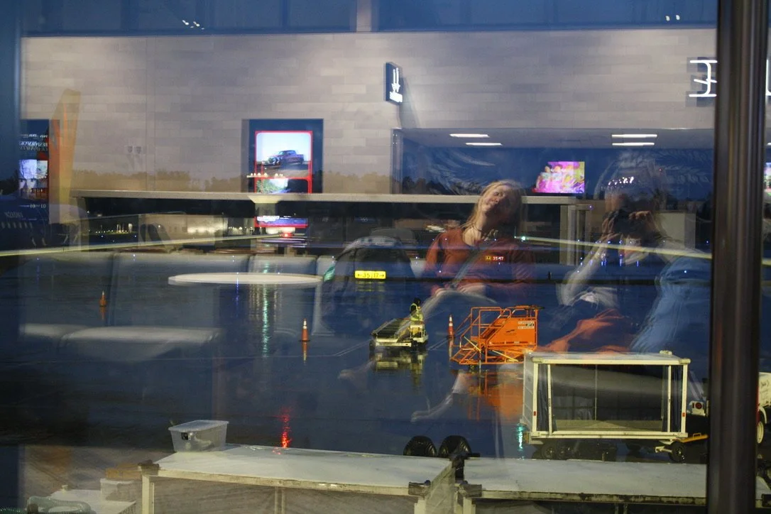  The reflections of Solena Davidson Carroll and Emma Taylor McCallum in the window over a view of the early morning tarmac at the Asheville Regional Airport. Asheville, N.C. on Oct. 10, 2026. (Echo/Emma Taylor McCallum) 