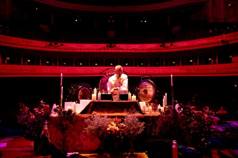 Person performing at a decorated altar with candles and flowers in a dimly lit auditorium.