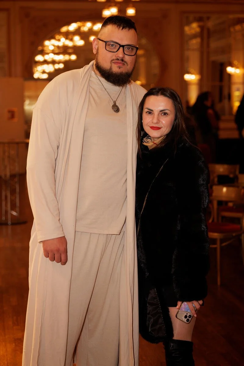 Two people posing together in a warmly lit indoor setting with elegant decor.