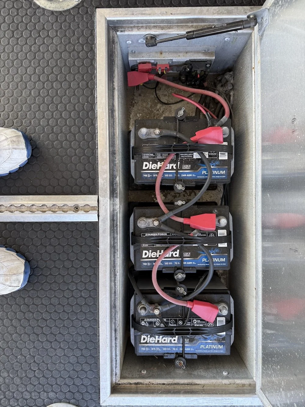 Three DieHard PLATINUM automotive batteries connected with black and red cables inside a metal compartment.