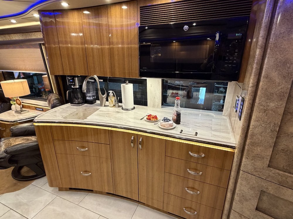 Kitchen area with wooden cabinets, marble countertop, microwave, coffee maker, paper towel holder, and plates.