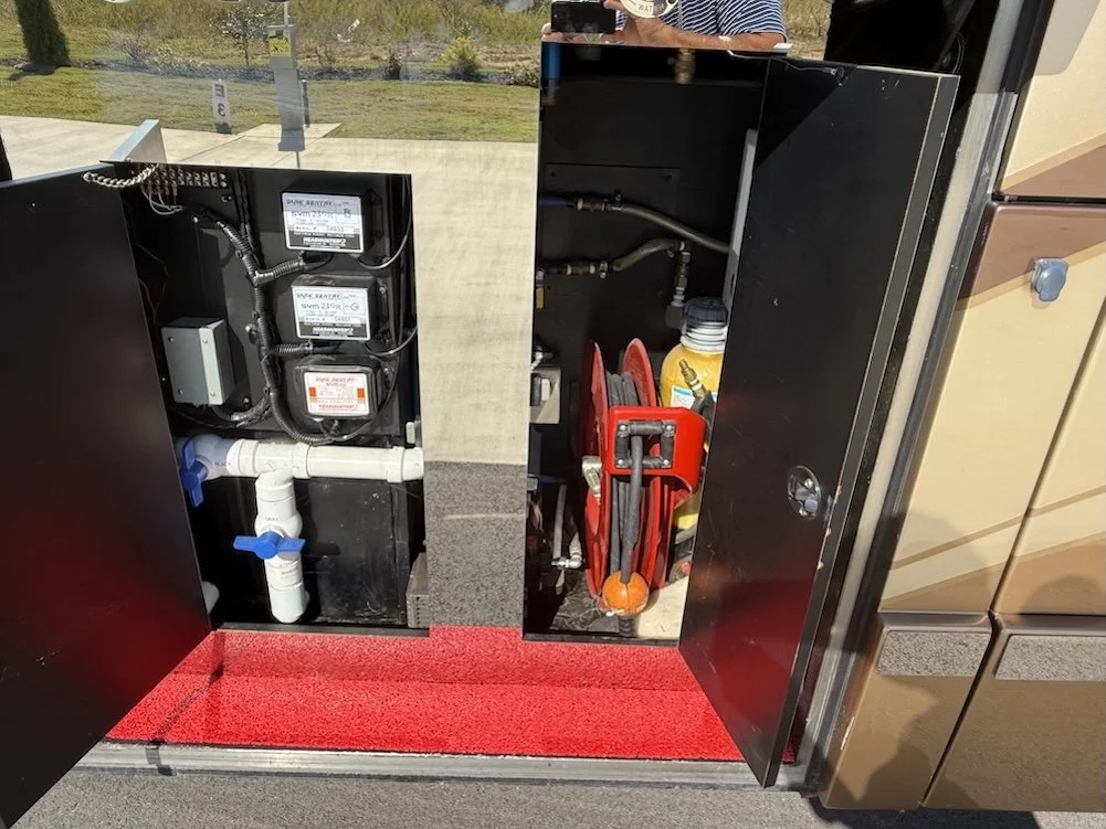 Open service bay displaying the coach utility hookups and water pump system.