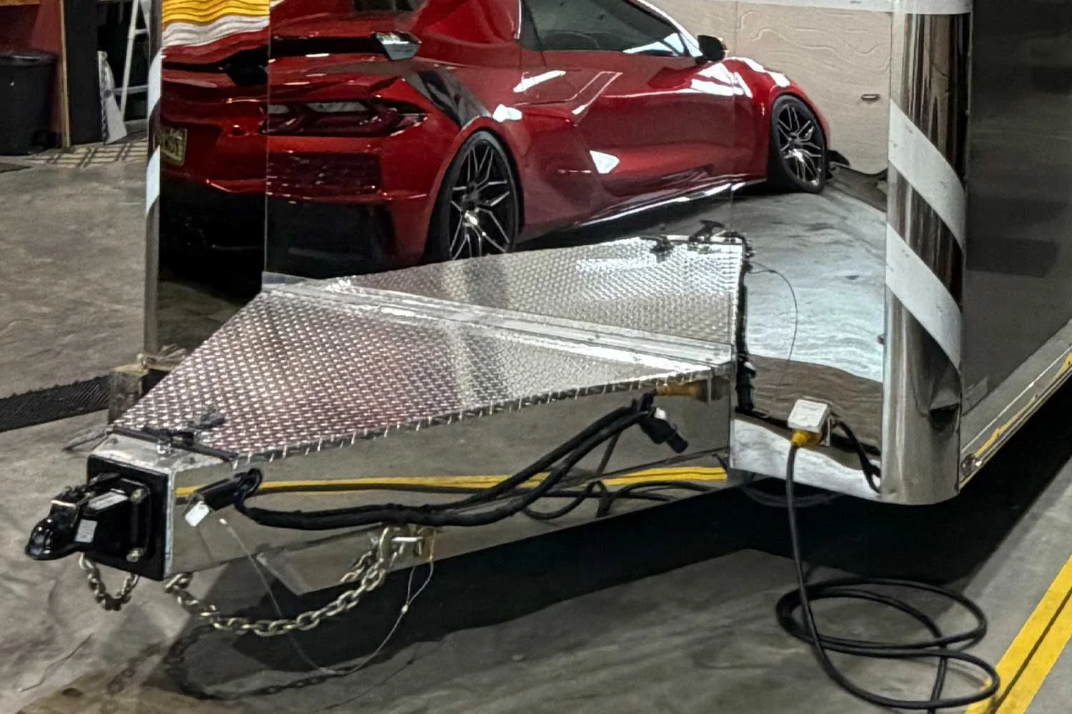 Trailer tongue with folding ramp near a parked Corvette